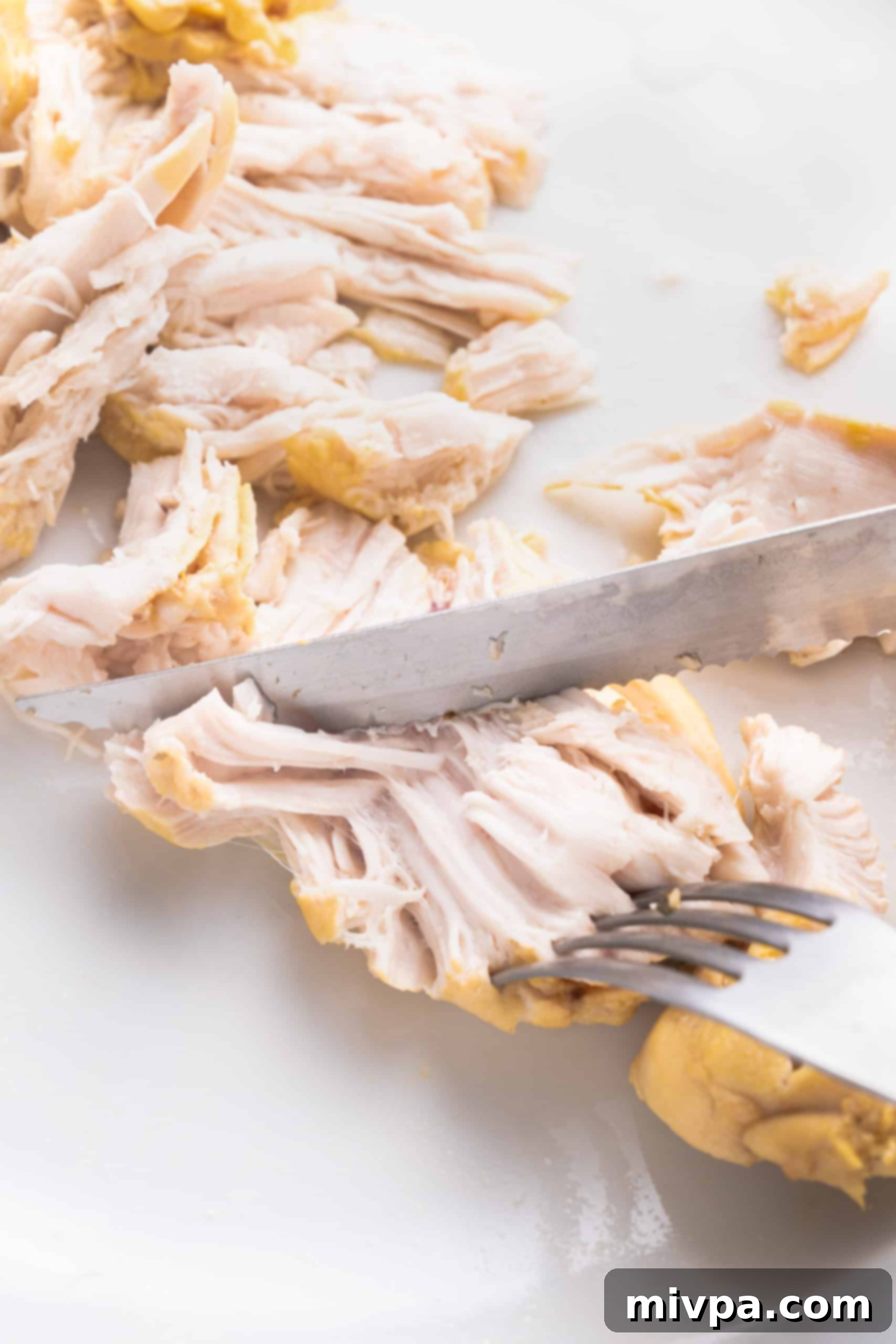 Shredding Chicken for Dairy-Free Chicken Noodle Soup (Gluten-Free) Hands using a fork and knife to shred cooked chicken breasts on a cutting board, preparing them for the gluten-free chicken noodle soup.