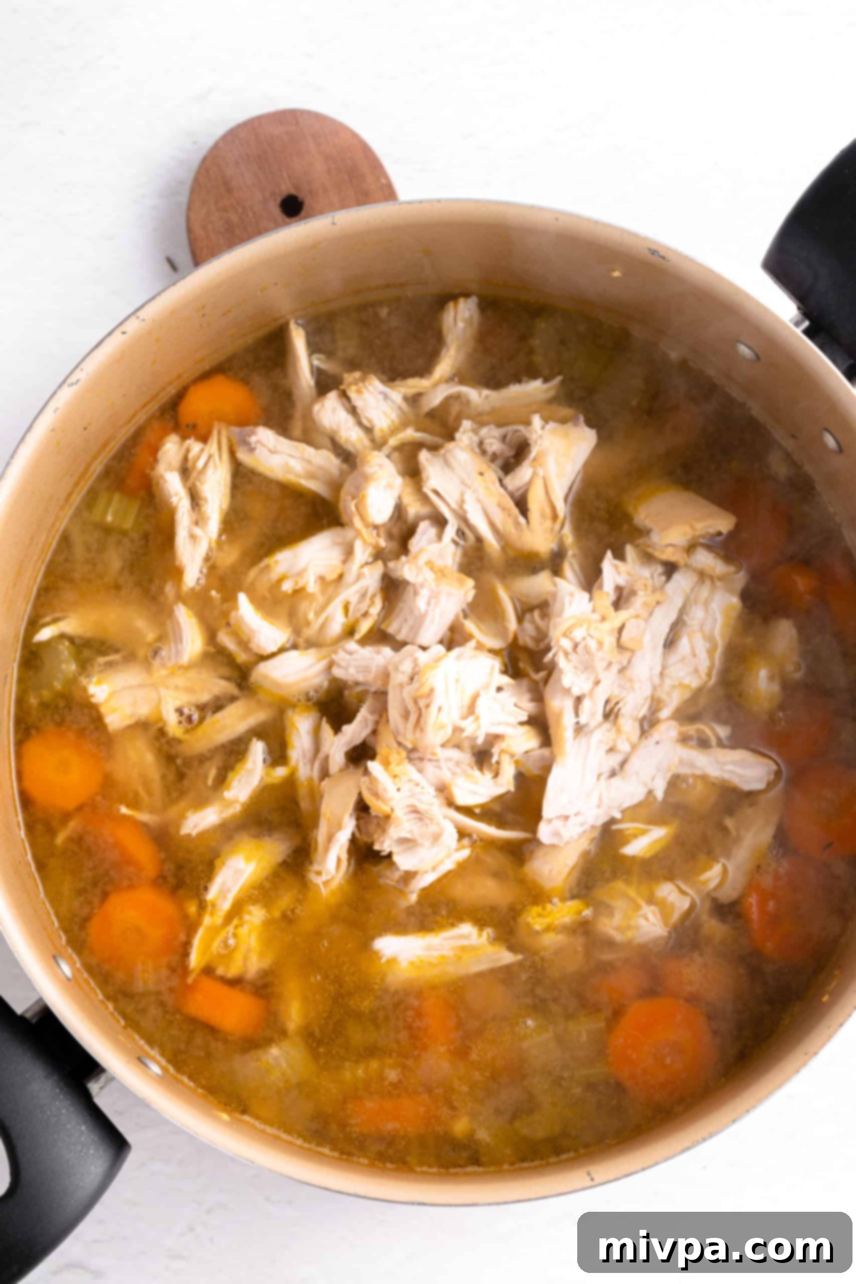 Returning Shredded Chicken to Gluten-Free Soup (Dairy-Free) Shredded chicken pieces generously added back into a rich bowl of soup, ready for the next steps in preparing gluten-free chicken noodle soup.