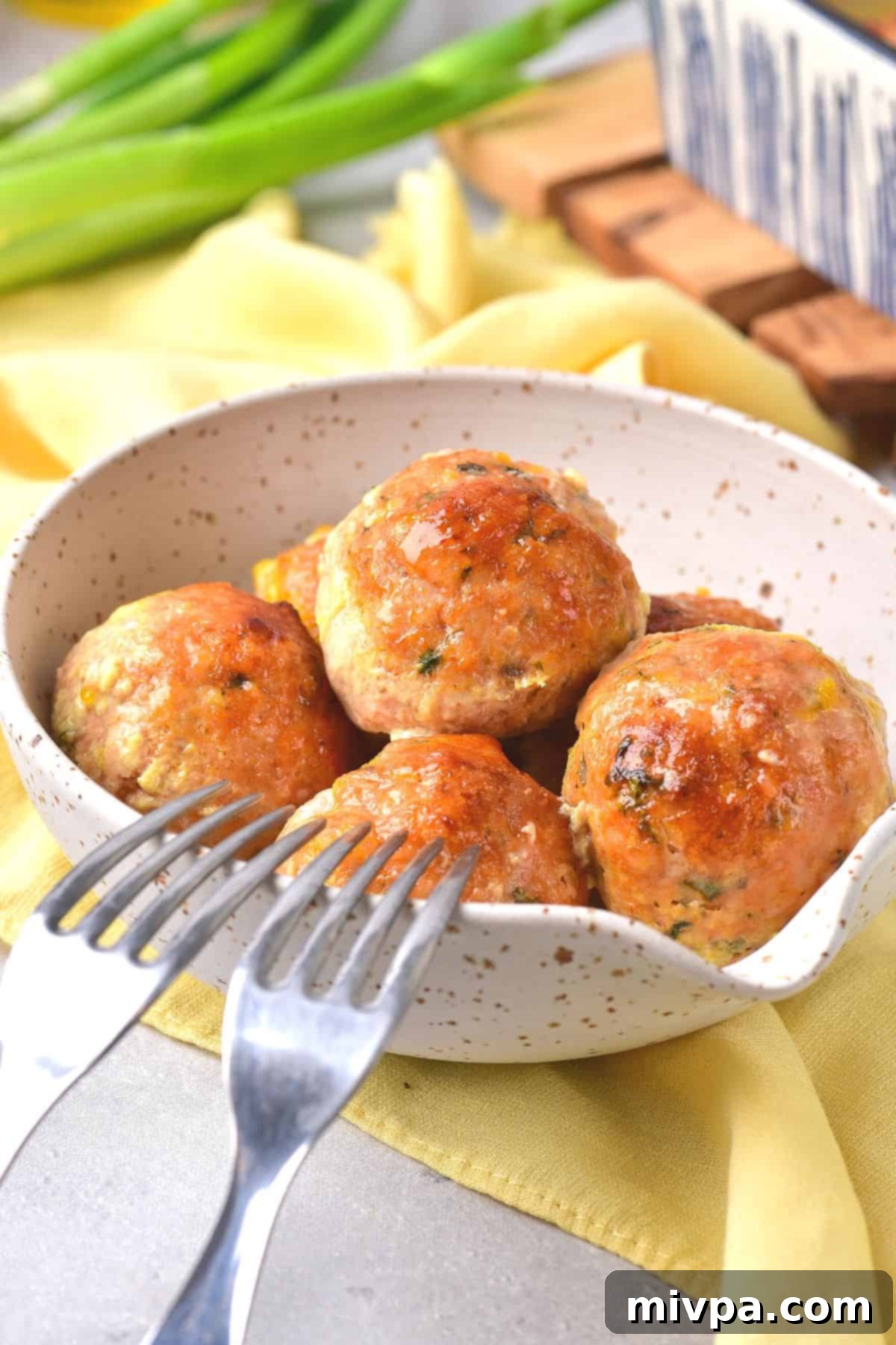Two forks resting on a bowl with chicken meatballs.