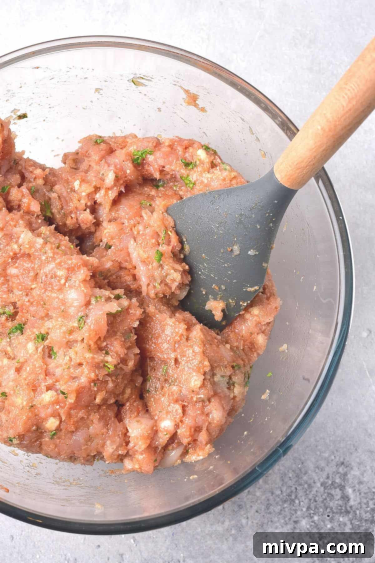 Using a spatula to mix chicken meatball mixture.