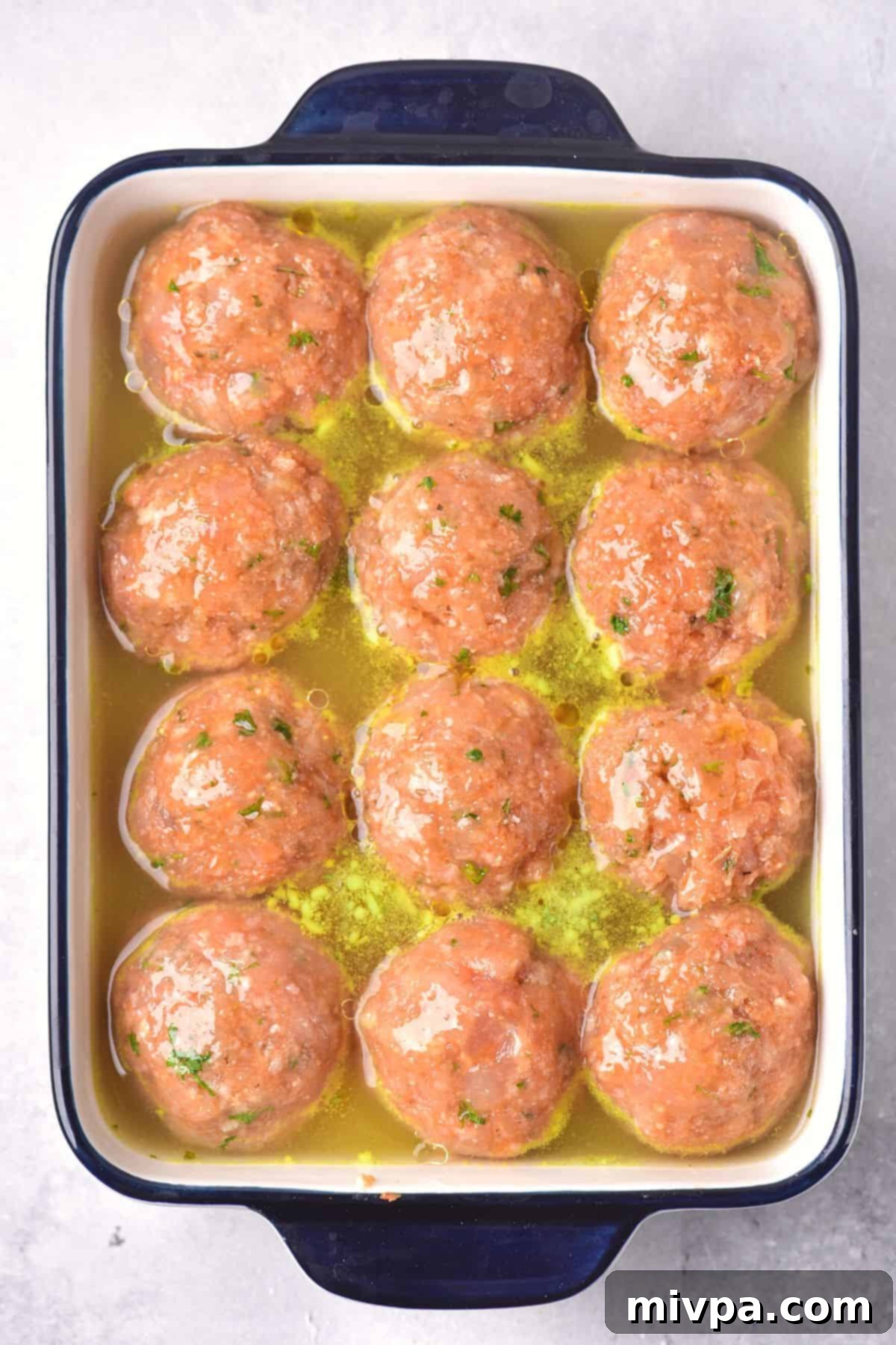 Uncooked chicken balls in broth in a baking dish.