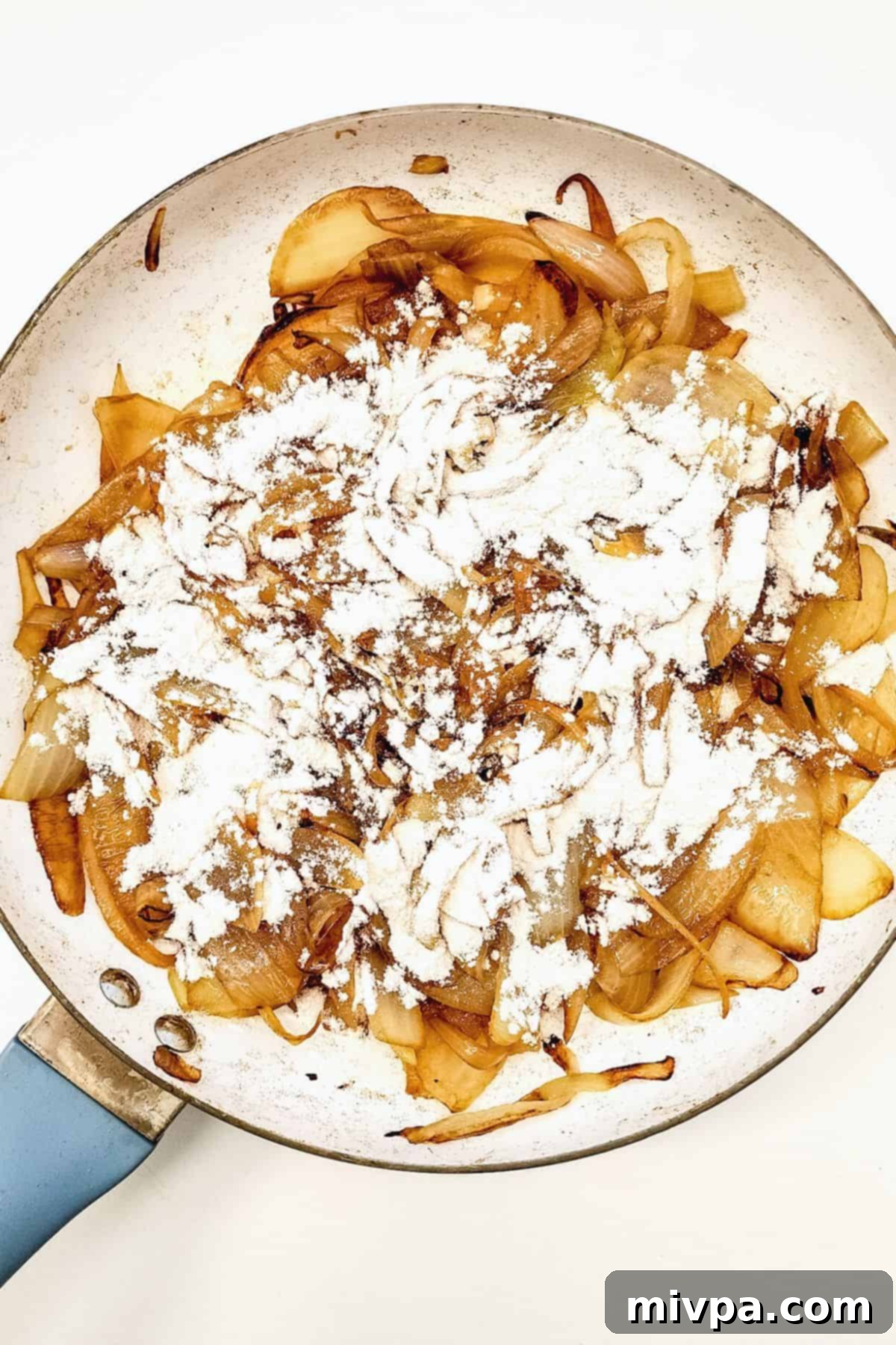 Flour sprinkled on top of caramelized onions in skillet.