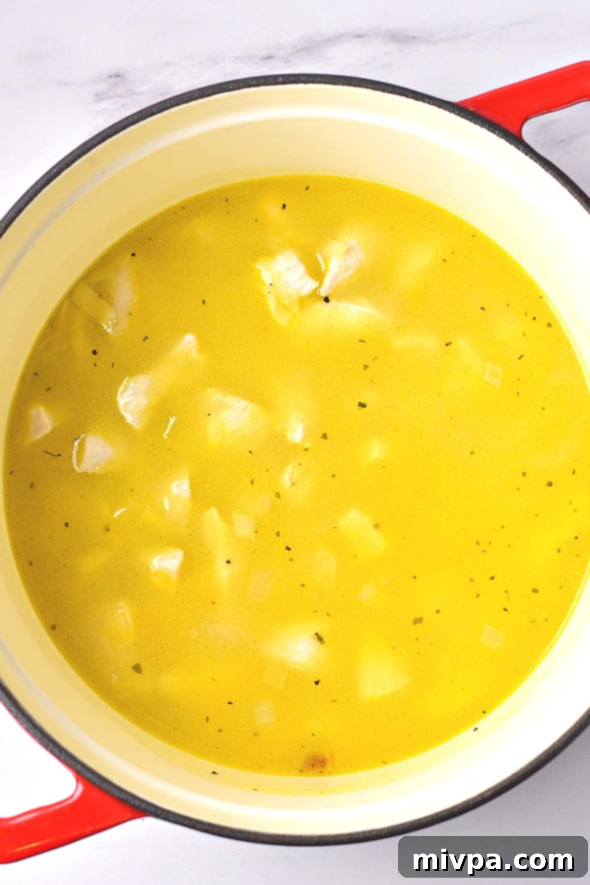 Gluten-Free Chicken Rice Casserole (Dairy-Free) Yellow mixture with chicken pieces, rice, and broth in a Dutch oven, covered and ready for baking.
