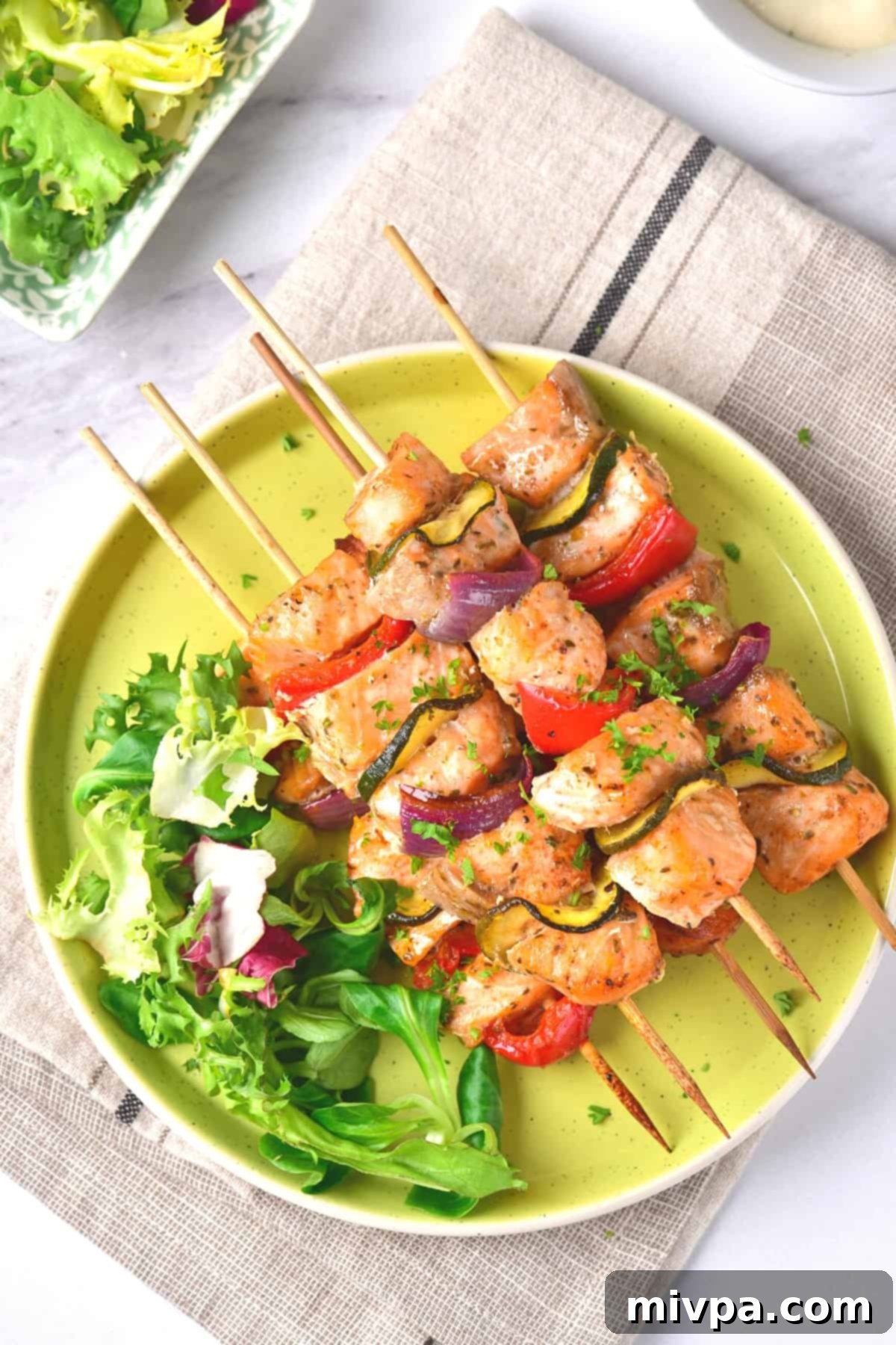 Salmon Kabobs in the Oven (Gluten-Free, Dairy-Free) A plate with baked salmon kabobs and salad greens on kitchen towel.
