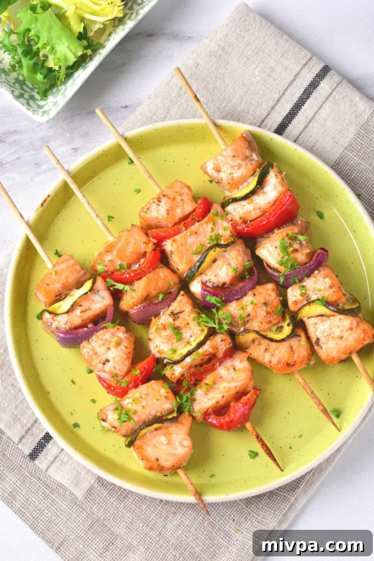 Baked Salmon Kabobs in Oven (Gluten-Free, Dairy-Free) Four salmon kebabs on a round green plate.