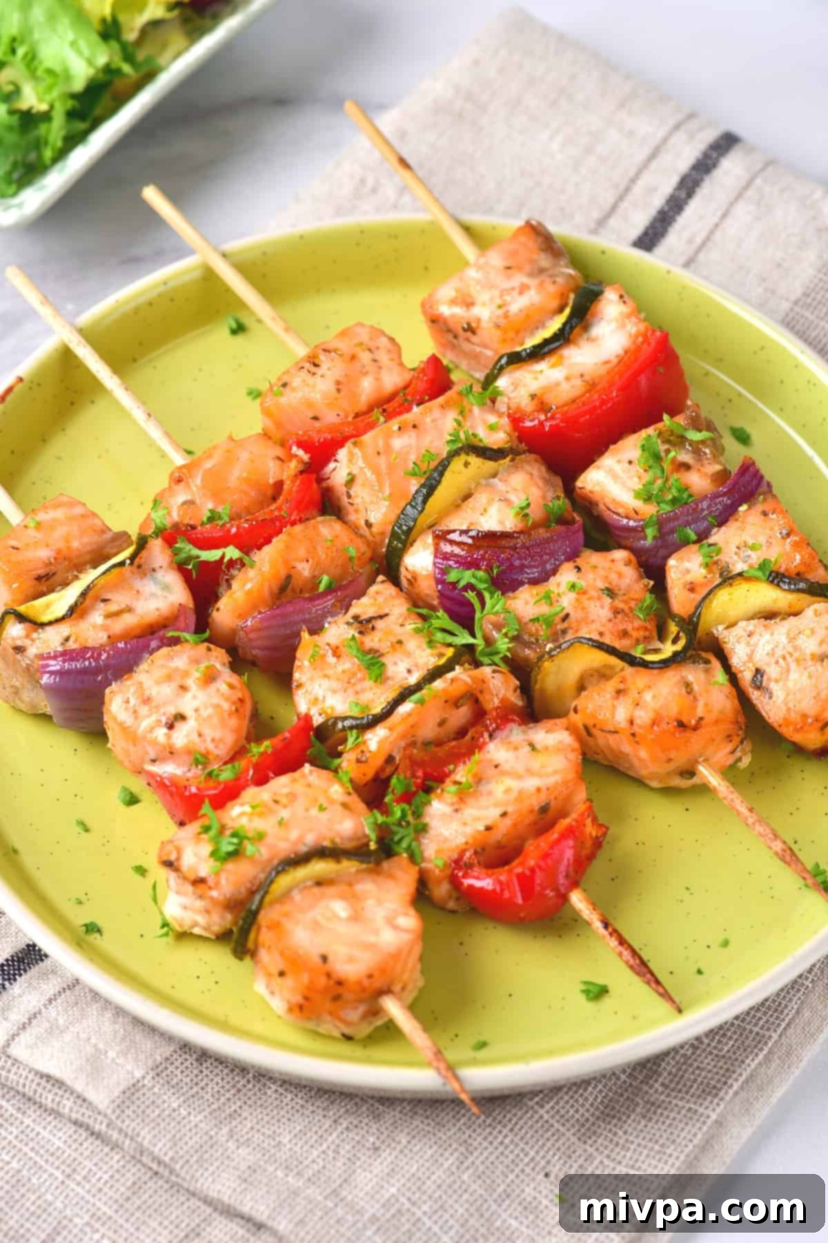 Baked Salmon Kabobs in the Oven (Gluten-Free, Dairy-Free) Up close view of salmon skewers on green plate.