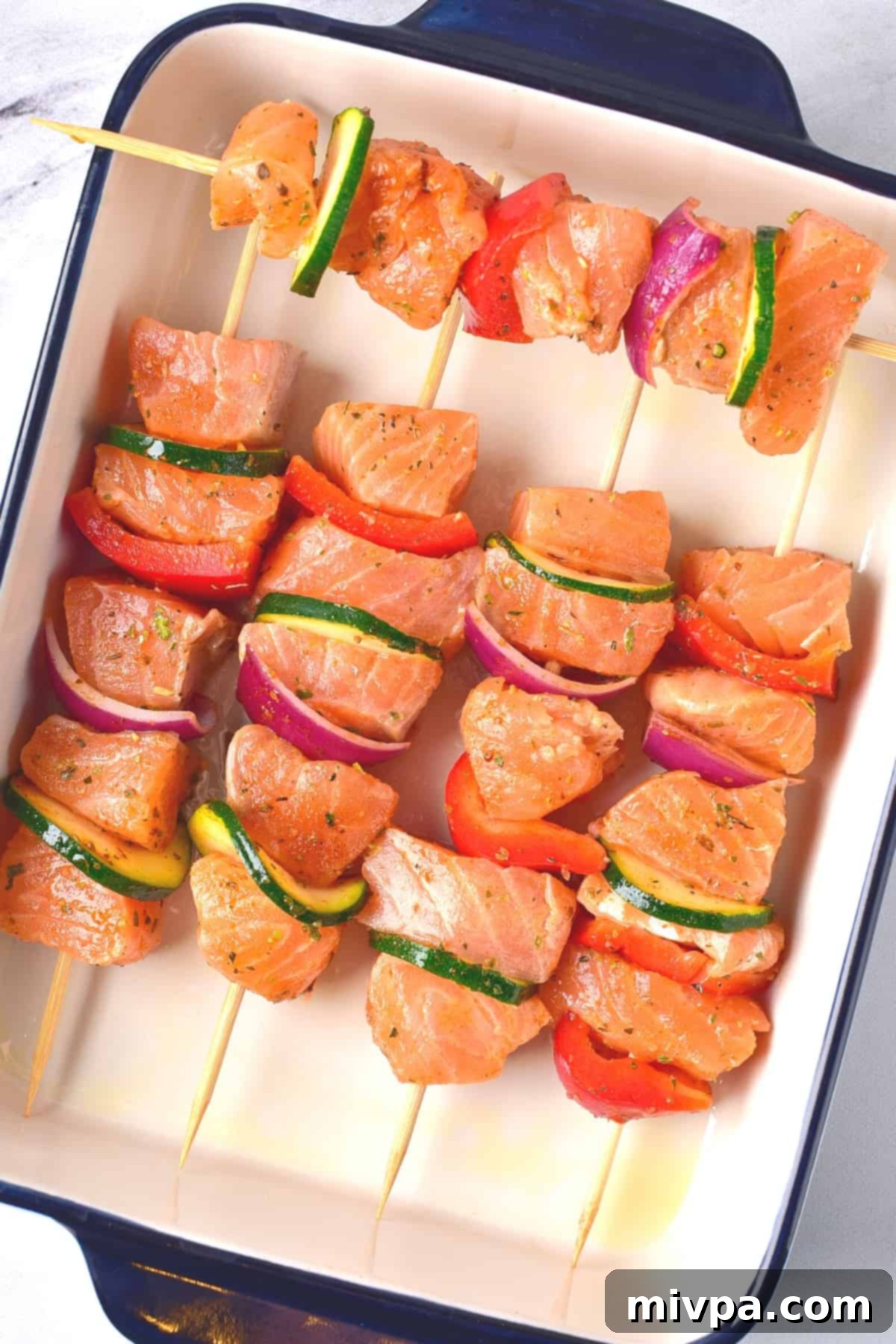 Baked Salmon Kabobs in the Oven (Gluten-Free, Dairy-Free) Uncooked salmon skewers in baking pan.