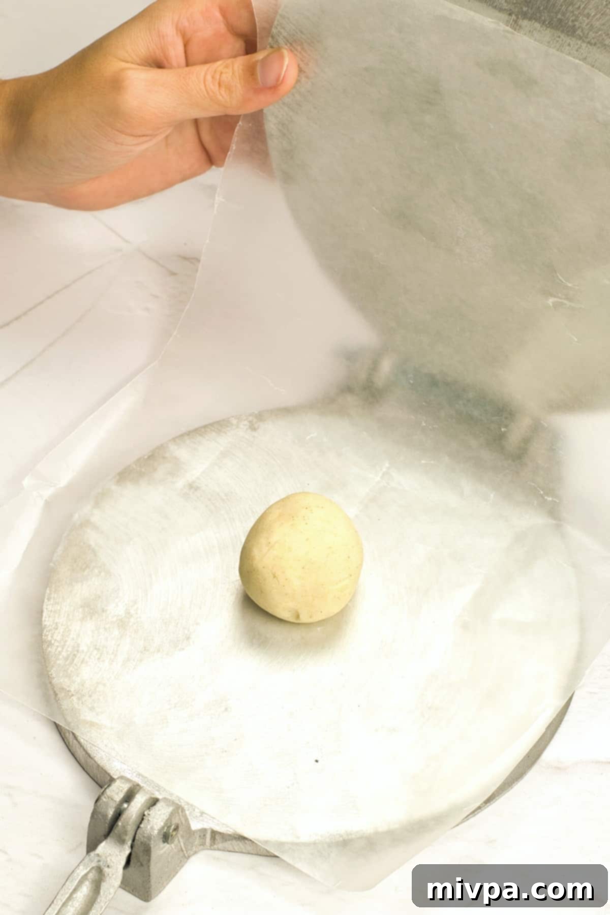 A small ball of dough on parchment-lined tortilla press.