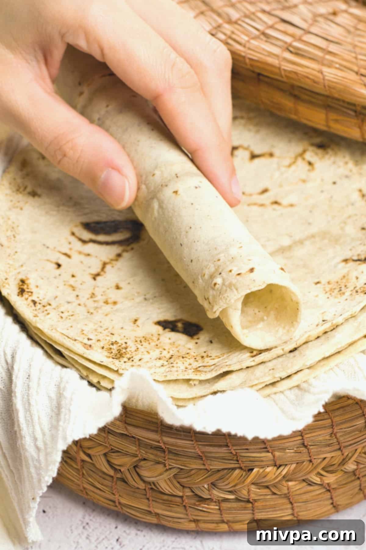 Rolling a homemade corn tortilla over a stack of tortillas.