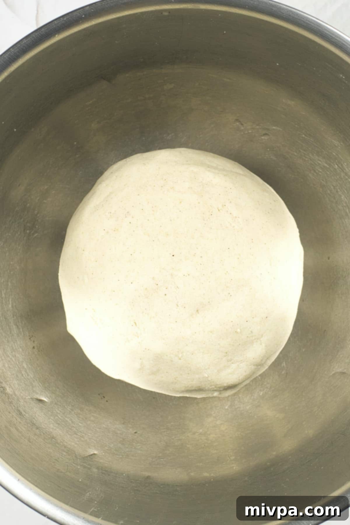 A ball of dough in a metal bowl.