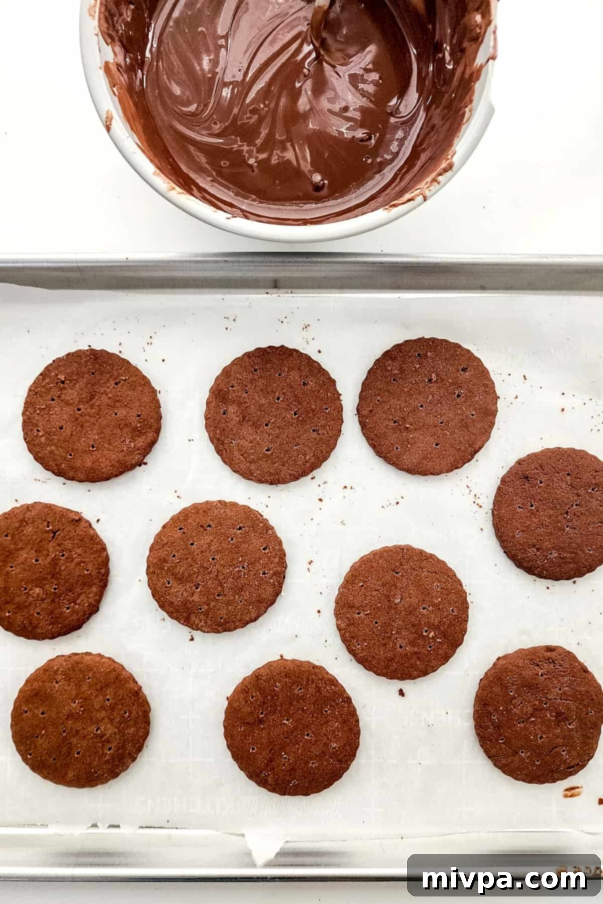 A baking sheet with cookies and a bowl of melted chocolate.