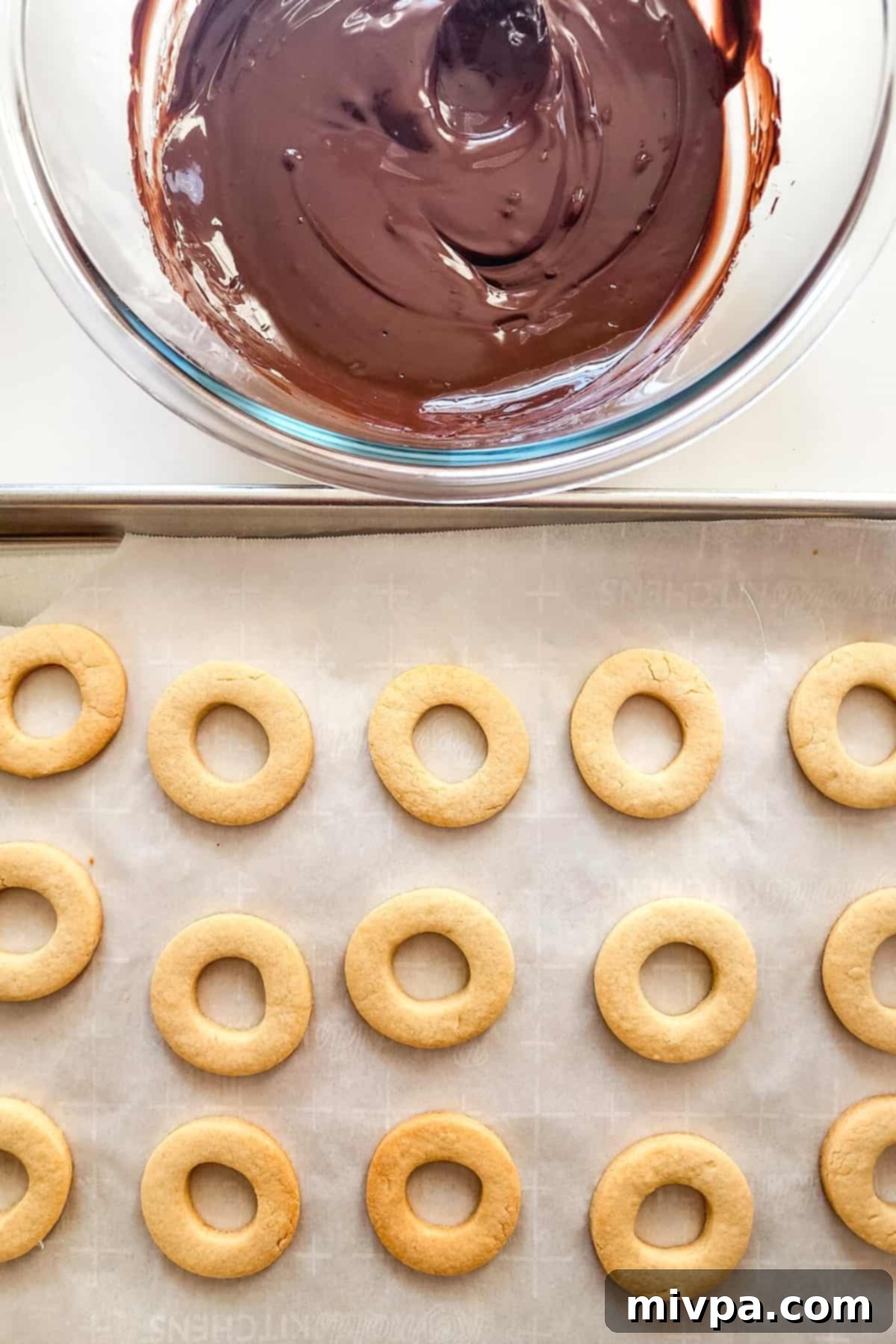 Gluten-Free Samoas Cookies (Dairy-Free) A parchment-lined tray with cookies and a bowl of melted chocolate.
