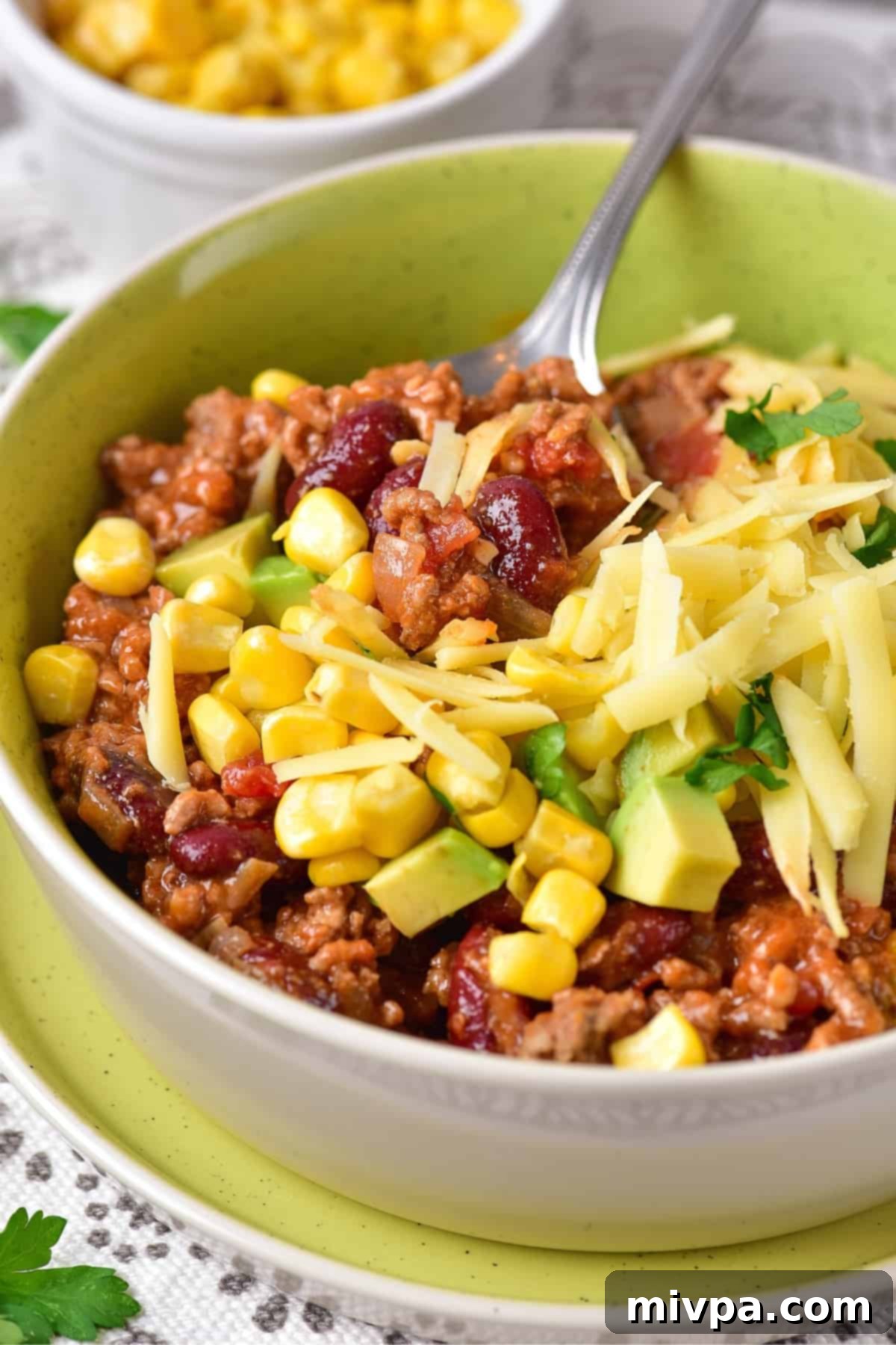 A spoon in a bowl of cheese-topped chili.