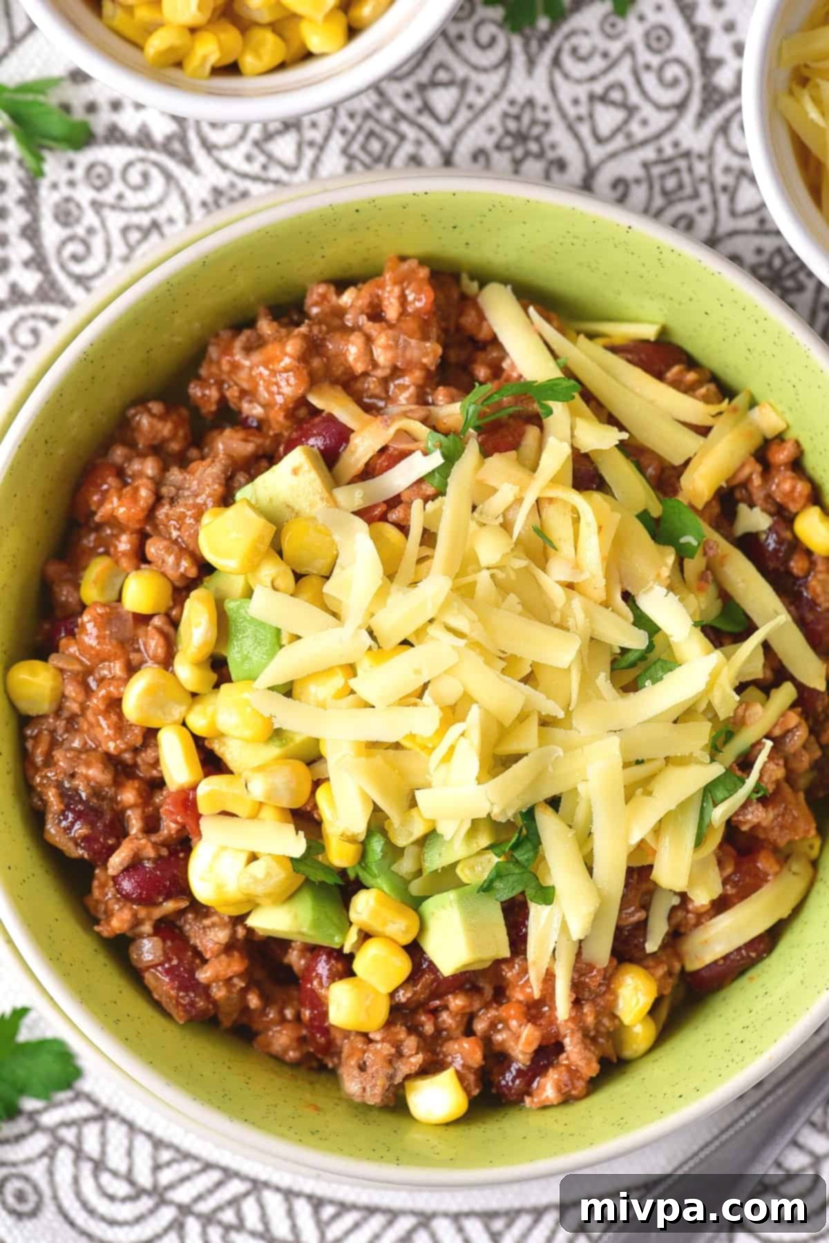 A bowl of chili topped with cheese, avocado and corn.