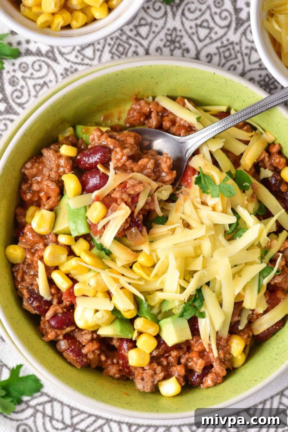 Top down view of a bowl of chili topped with cheese, avocado and corn.