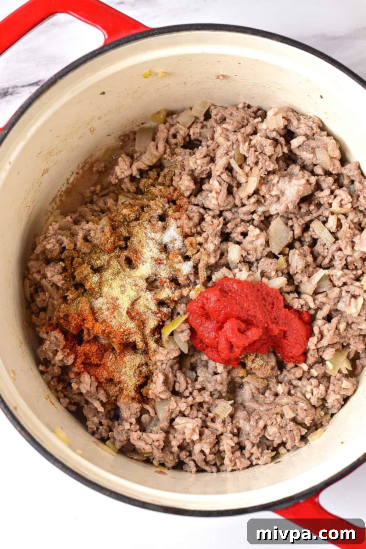 Cooked ground beef and tomato paste in a pot.