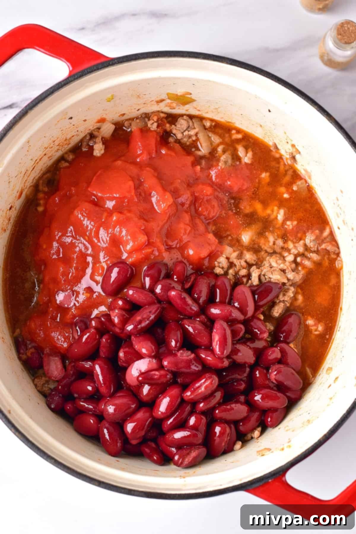 A large Dutch oven with red kidney beans, chopped tomatoes and minced beef.
