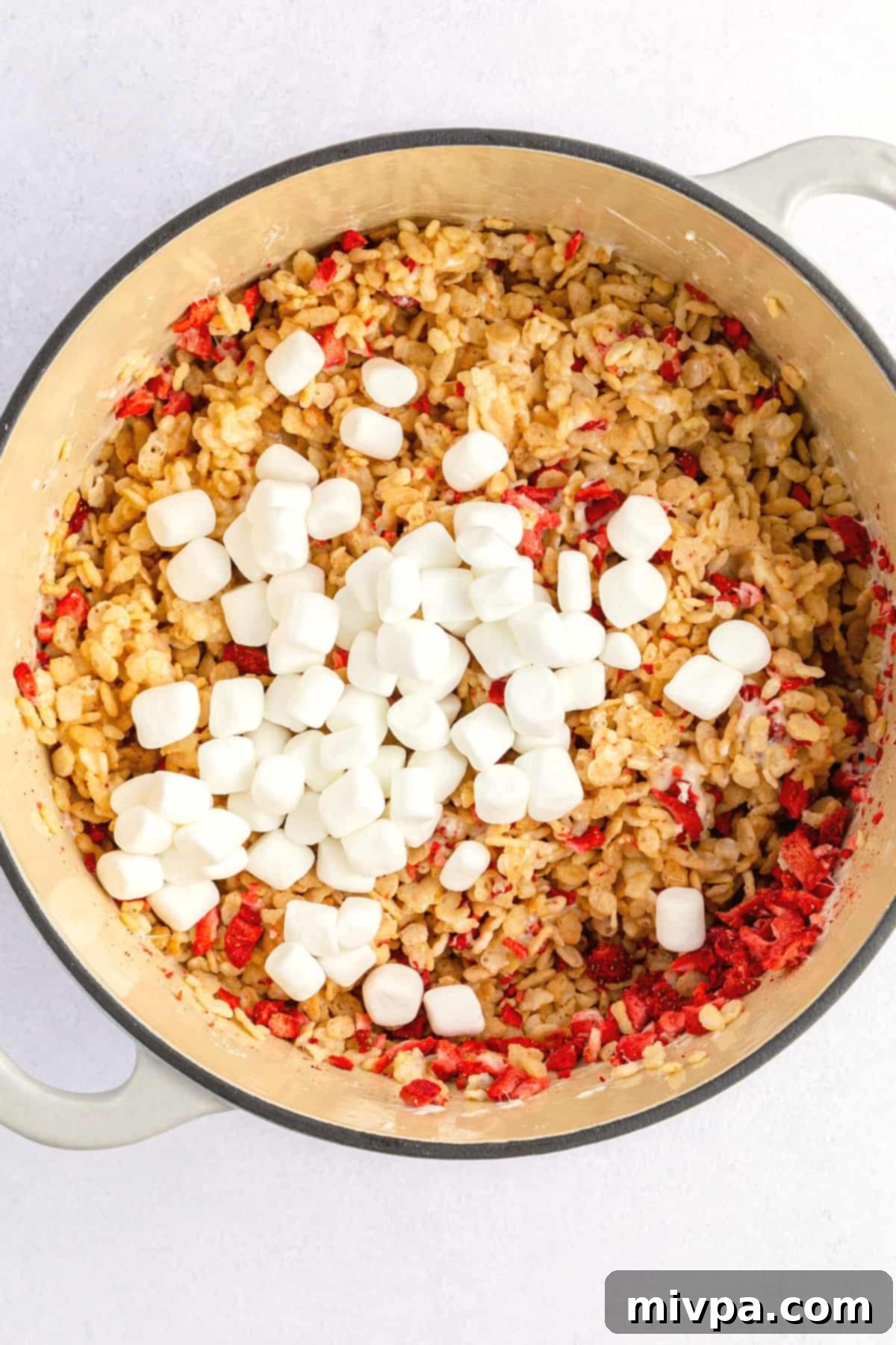 A big pot filled with cereal mixture topped with mini marshmallows, ready to be folded.