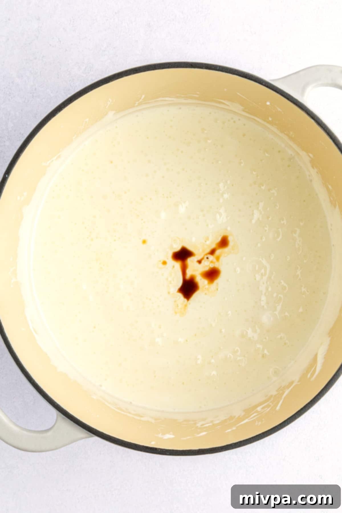 A pot of melted marshmallows with a swirl of vanilla extract being mixed in.