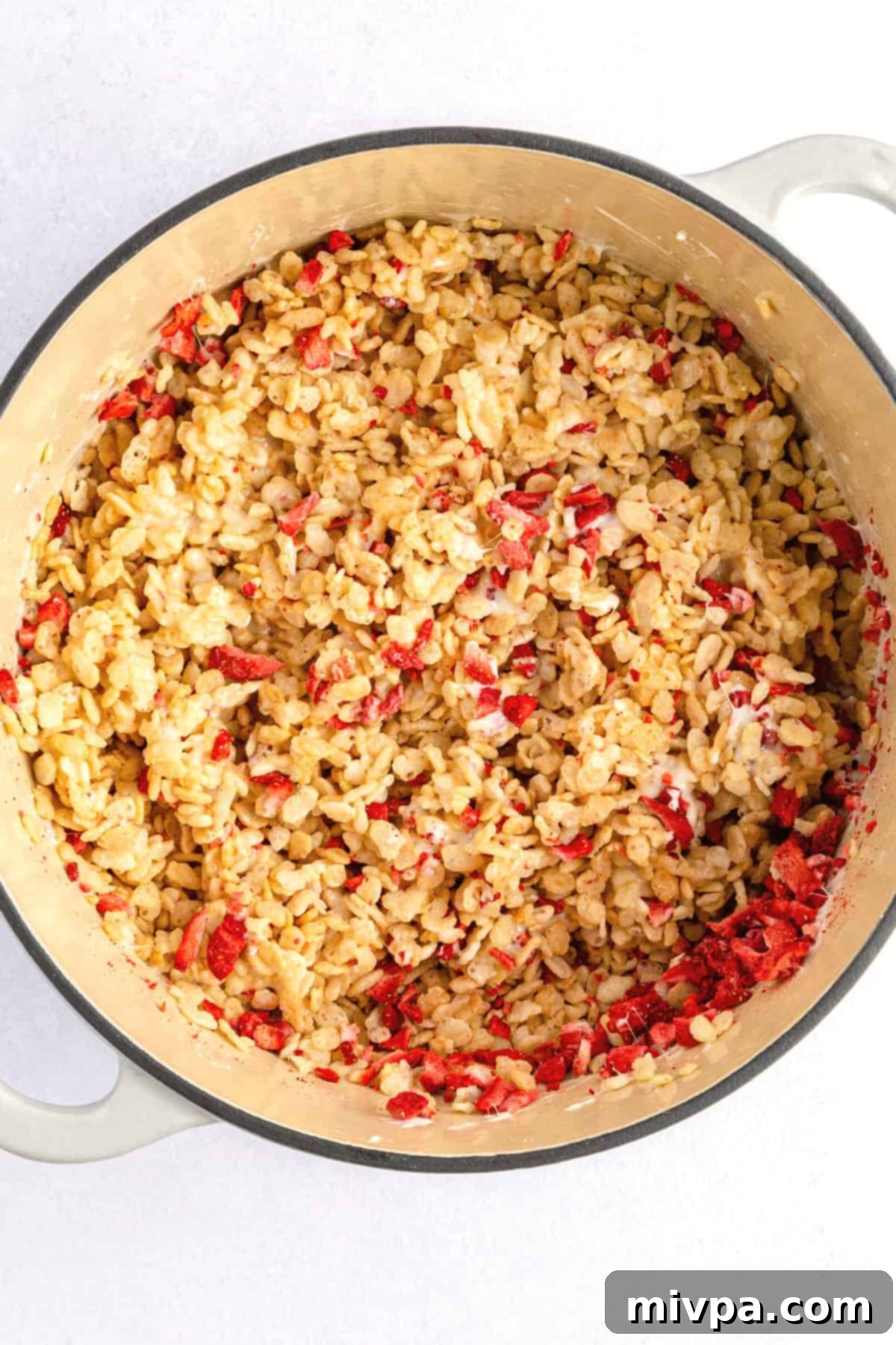 Rice cereal mixture with freeze-dried strawberries in a Dutch oven, being folded.