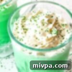 Easy Homemade Gluten Free Vegan Shamrock Shake 2 Close-up of a creamy green shamrock shake topped with whipped cream and green sprinkles in a glass.