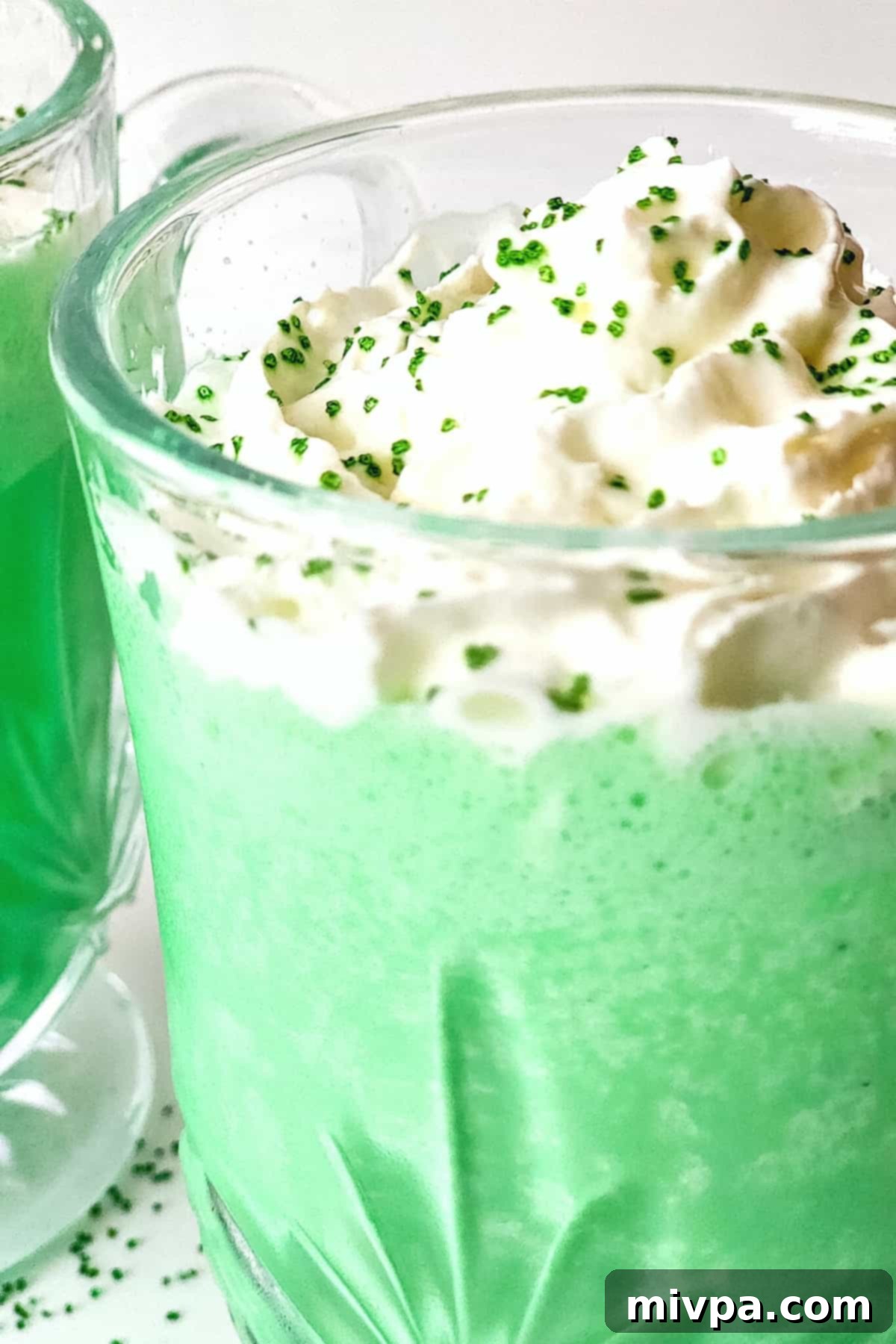 Homemade Vegan Shamrock Shake Recipe (Gluten-Free) Close-up view of a single vegan shamrock shake in a tall glass, garnished with whipped cream and green sprinkles.