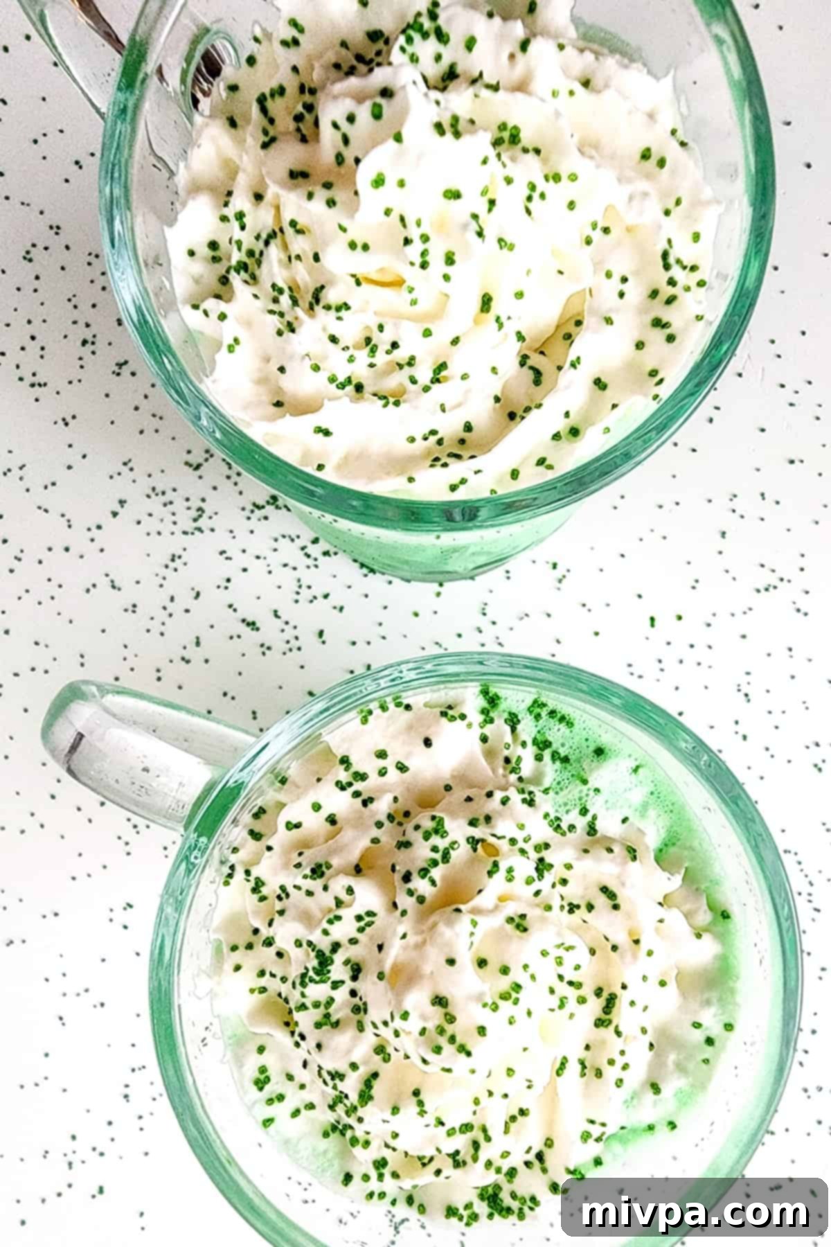 Homemade Vegan Shamrock Shake (Gluten-Free) Two glass cups filled with vegan shamrock shakes, topped with whipped cream and green sprinkles, ready to be enjoyed.
