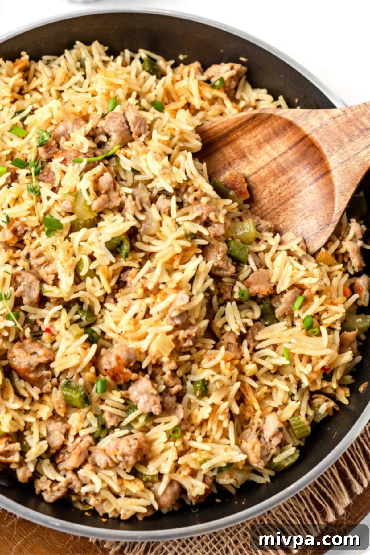 A wooden spoon scooping into a skillet of rich, flavorful Cajun dirty rice, ready to be served.