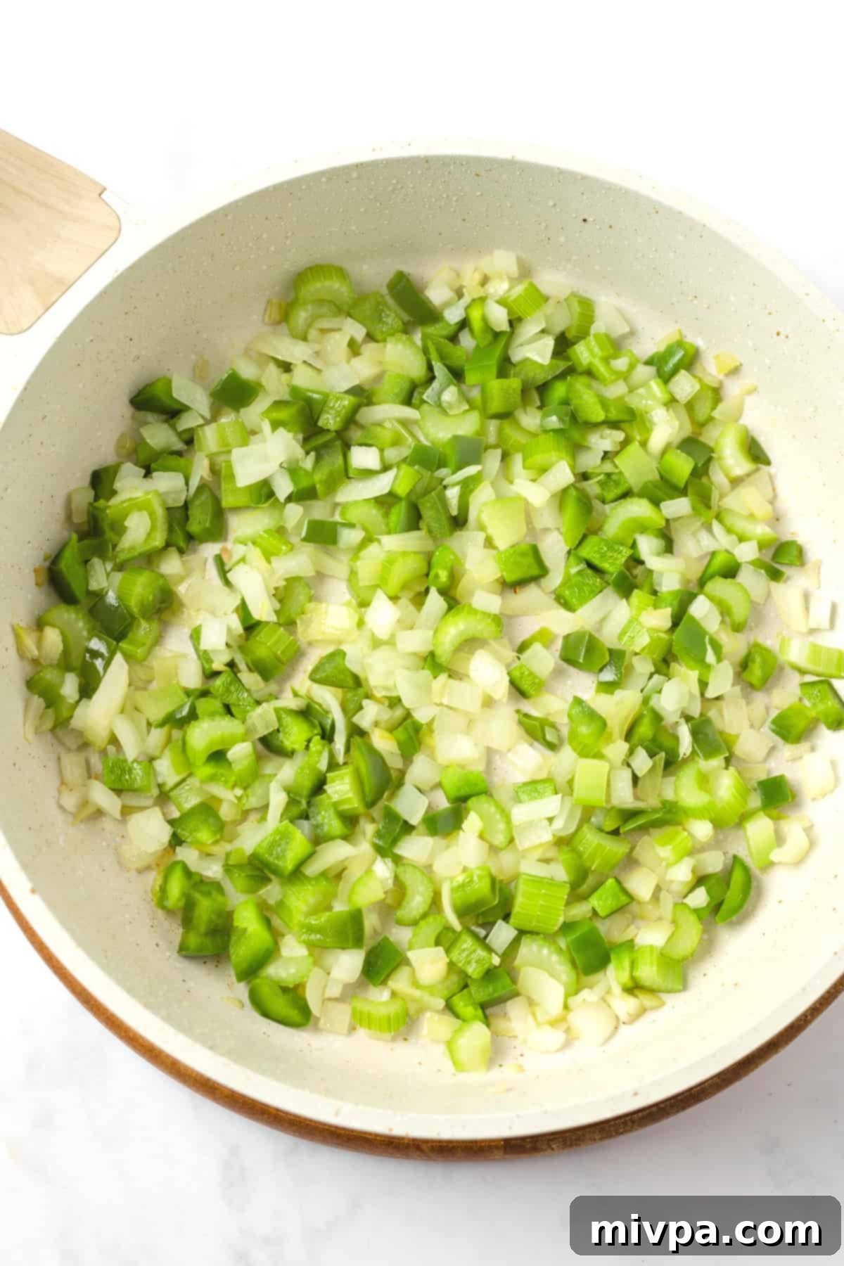 Diced celery and onions cooking in a skillet, softening and becoming translucent.