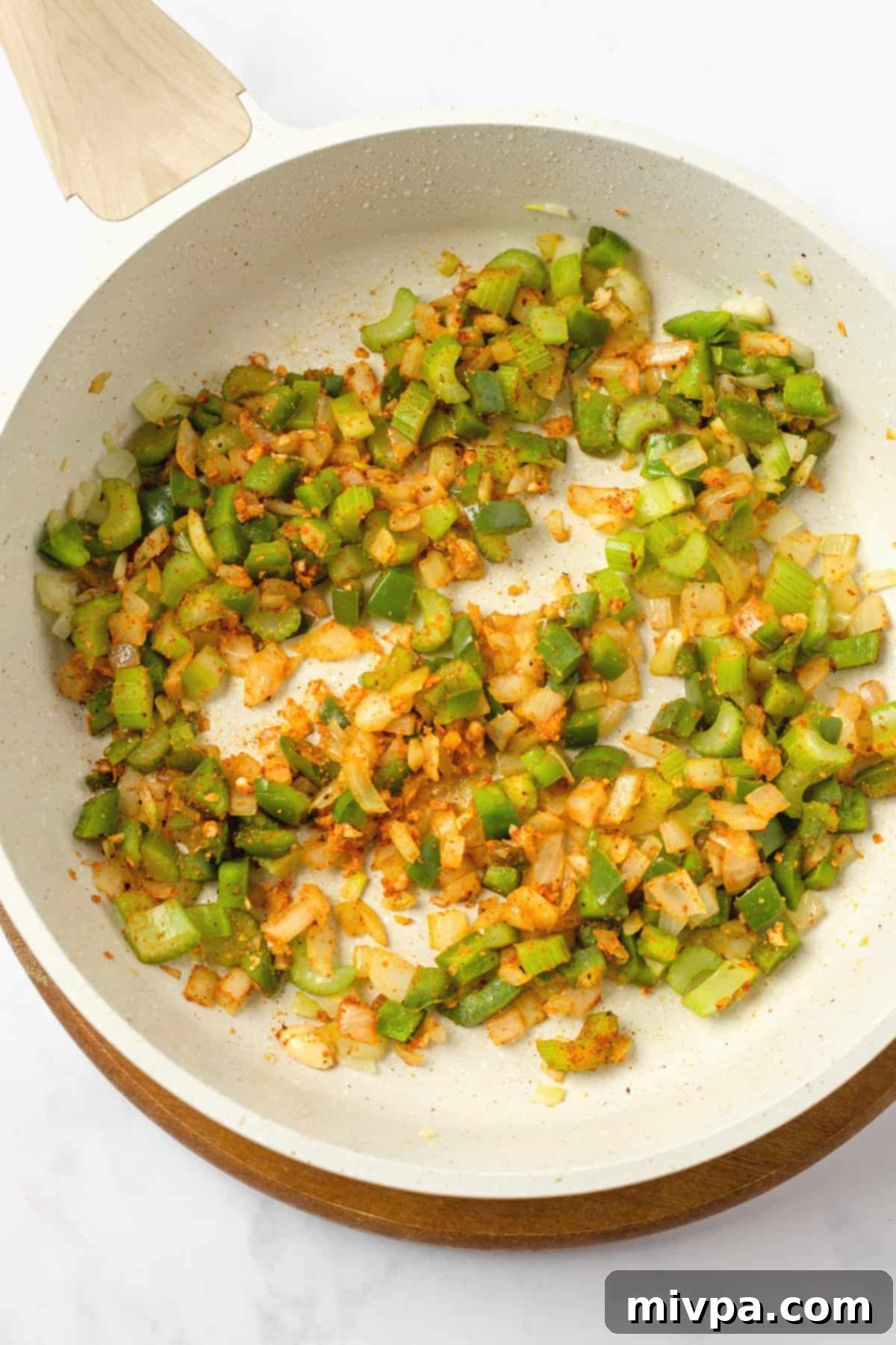 Sautéed vegetables in a skillet with added spices and minced garlic, releasing their aromas.