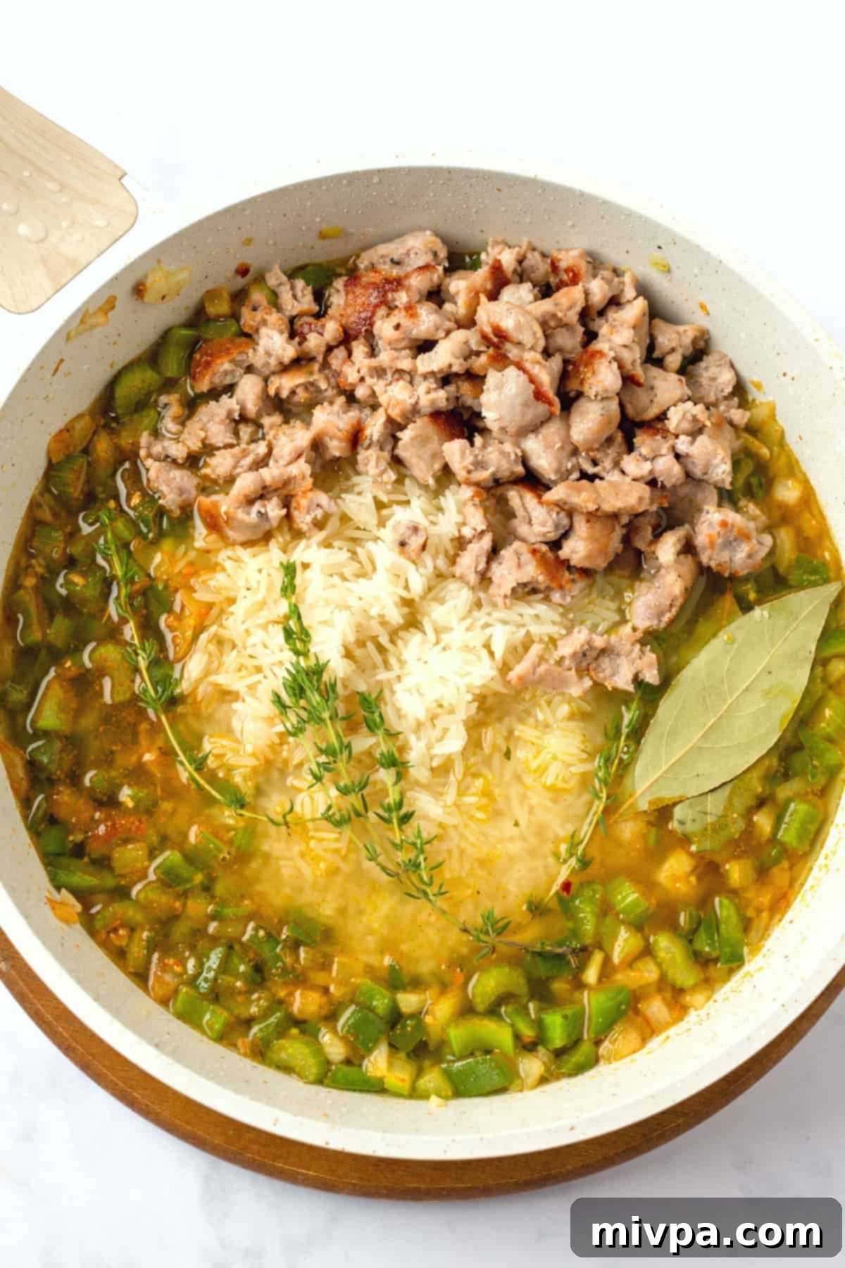 All the cooking ingredients, including rice, broth, herbs, and cooked sausage, combined in a skillet before simmering.