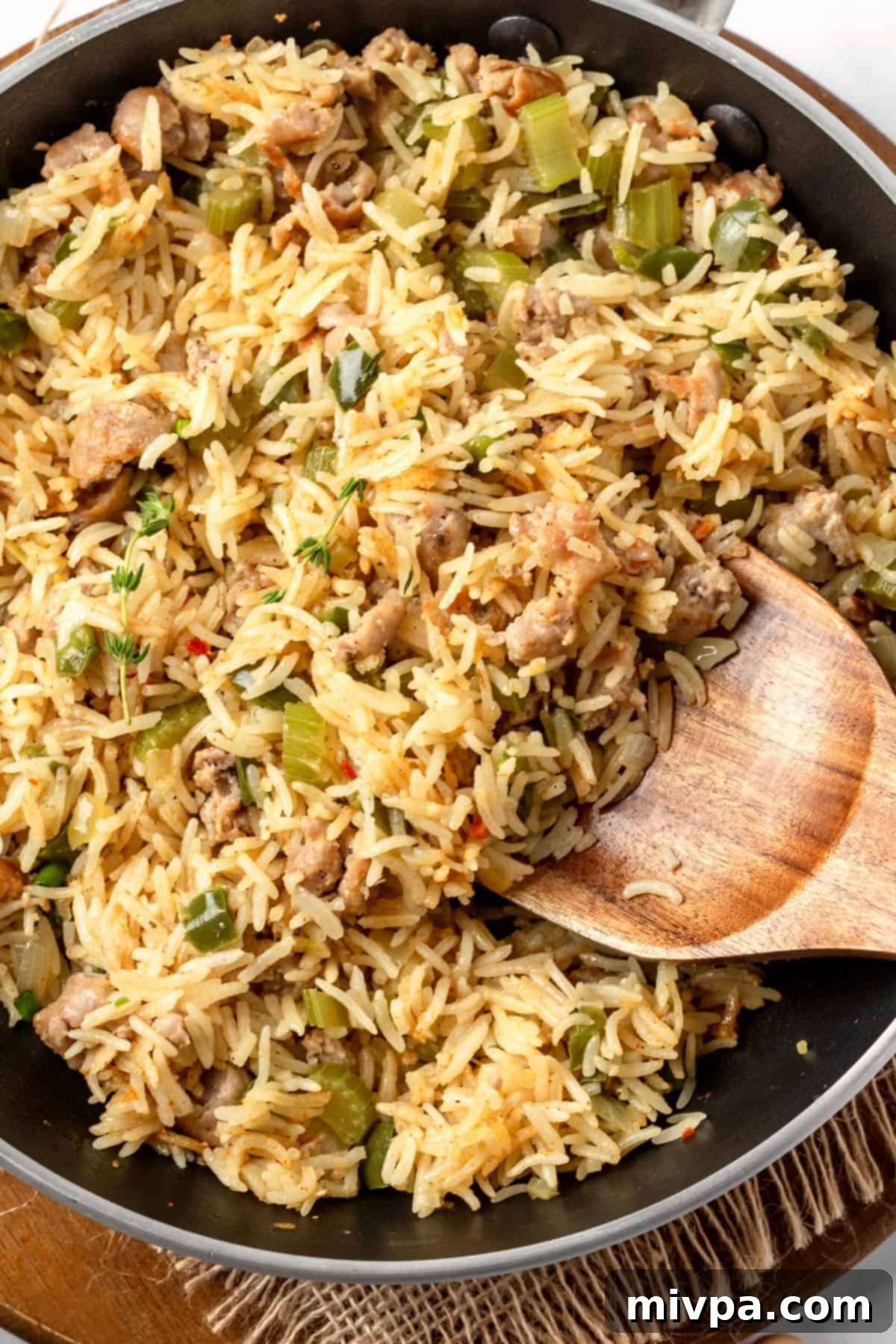 Scooping out fluffy, perfectly cooked dirty rice with a wooden spoon from a skillet.