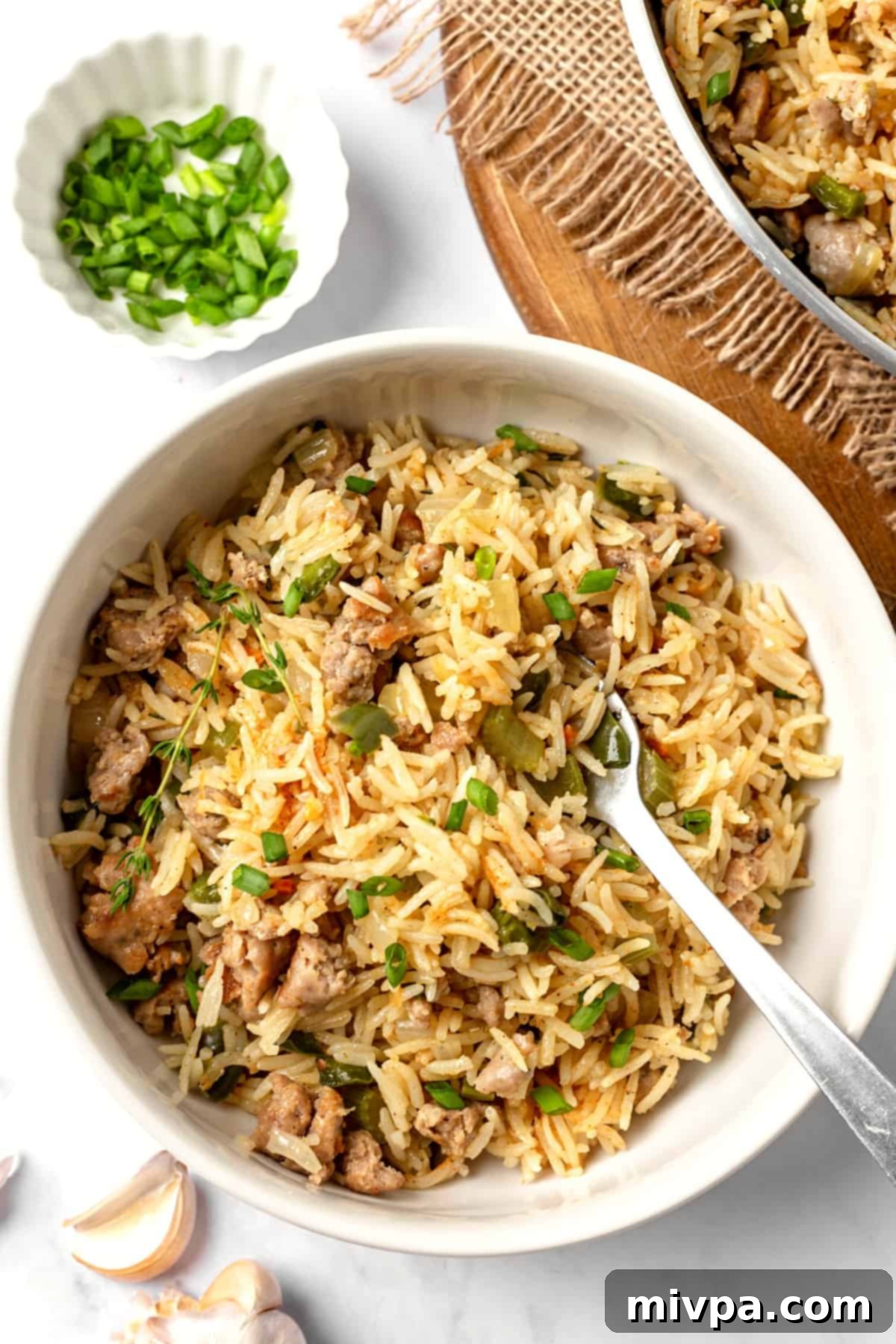 A wooden spoon in a bowl of beautifully garnished sausage dirty rice, ready to eat.