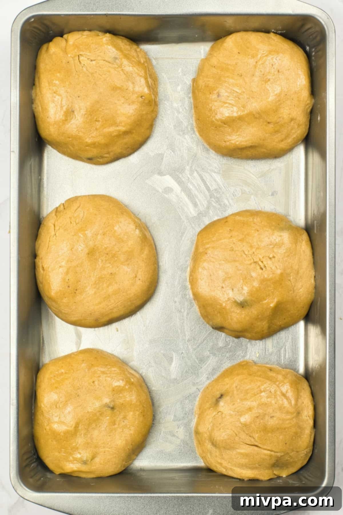 Round balls of gluten-free bread dough arranged in a greased metal baking pan.