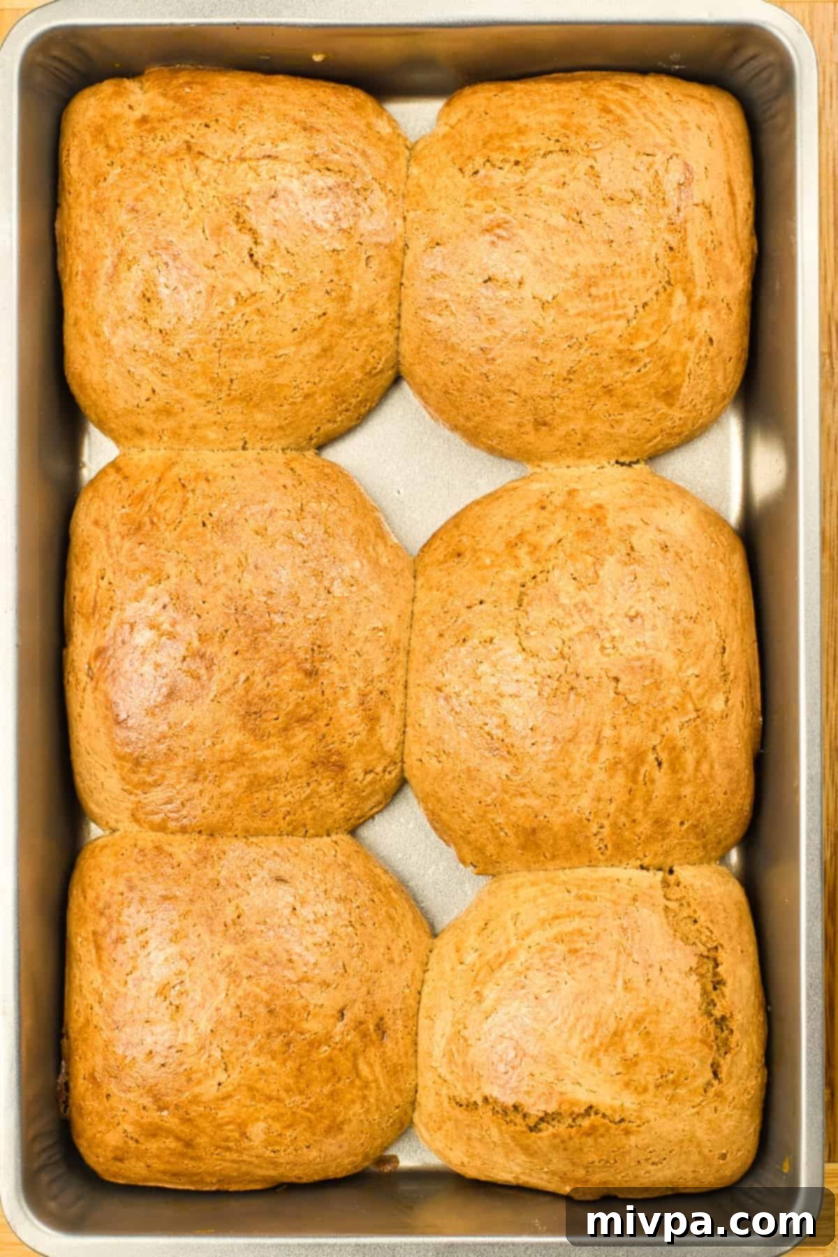 Freshly baked gluten-free hot cross buns in a metal baking pan, golden brown and puffed.