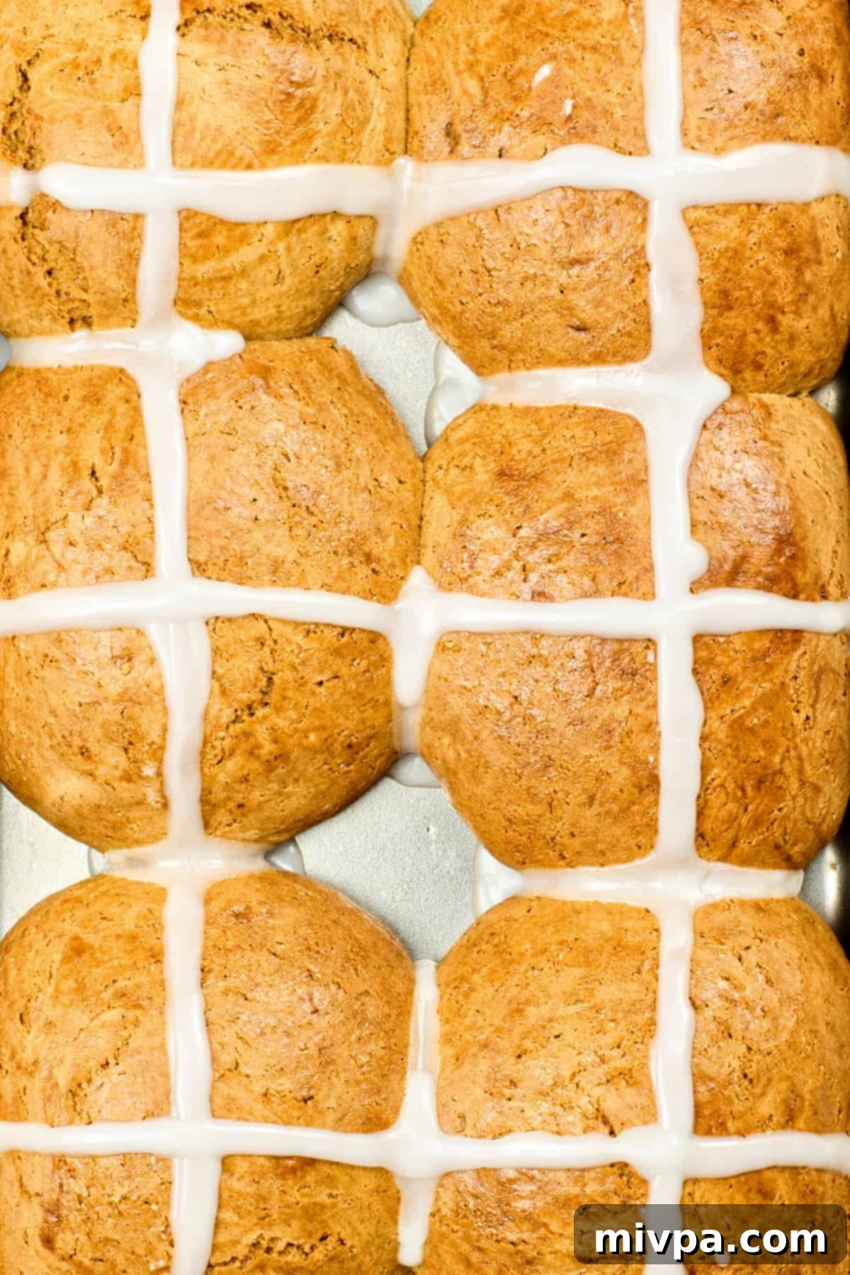 Freshly baked gluten-free hot cross buns, with piped icing crosses, cooling in a metal pan.
