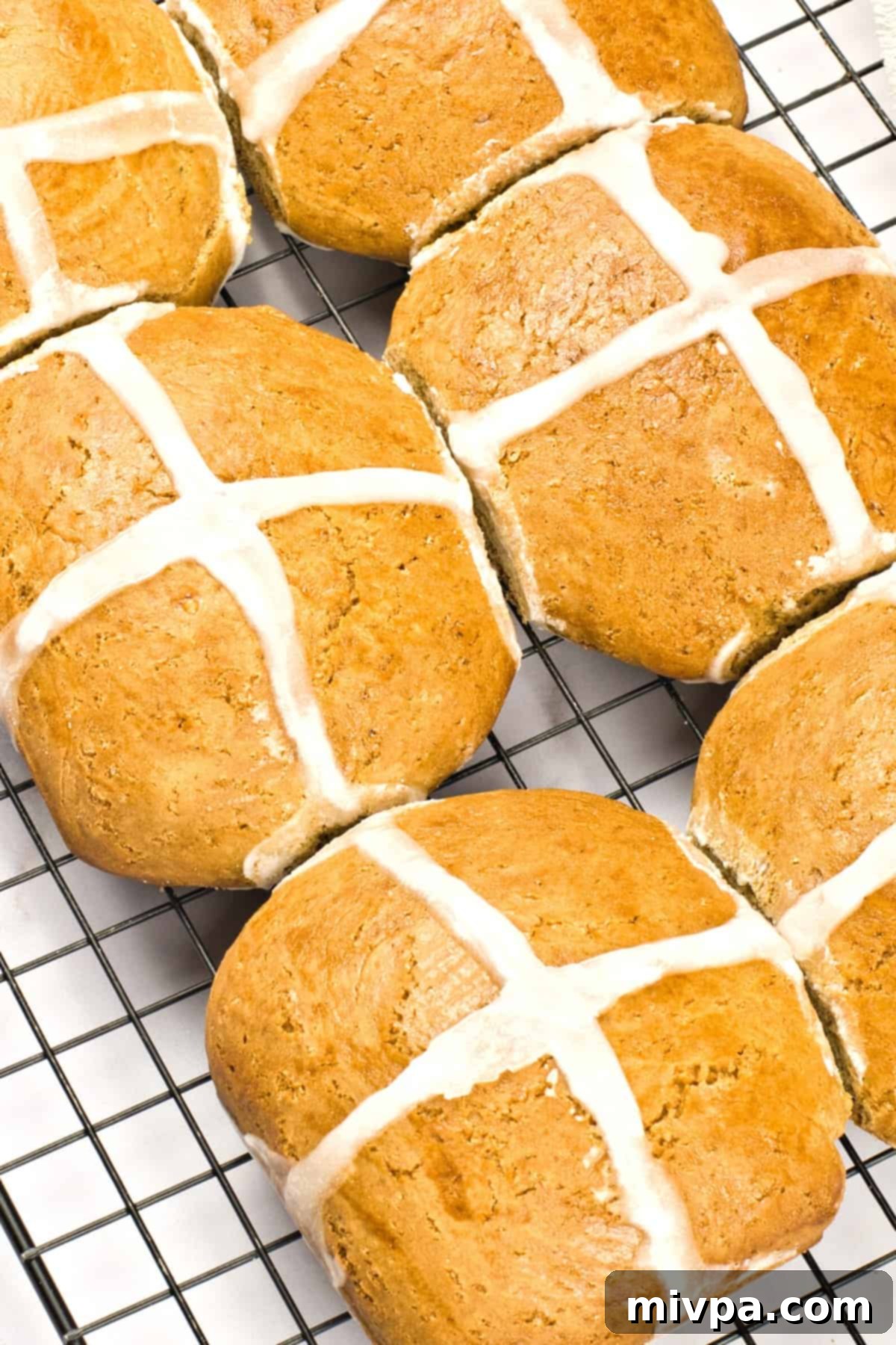 Close-up shot of a single, perfectly glazed gluten-free hot cross bun on a cooling rack.