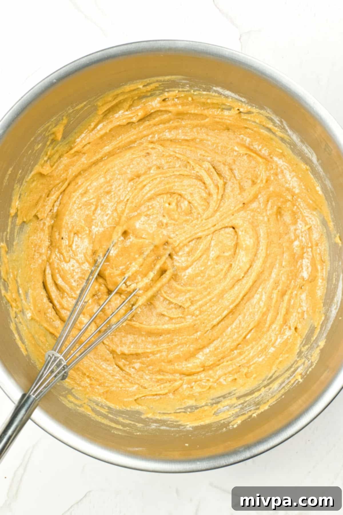 Whisking wet ingredients into dry ingredients to form gluten-free dough in a metal bowl.