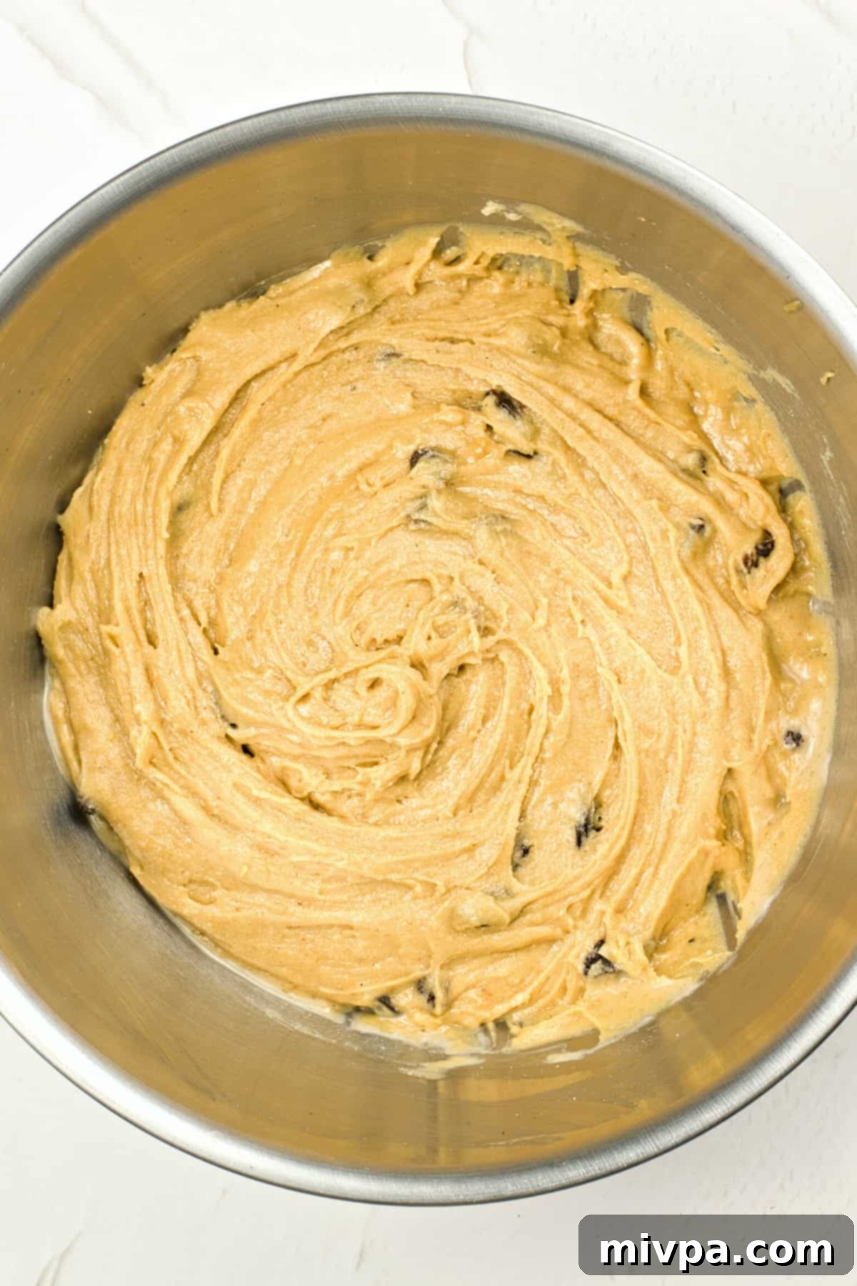 Gluten-free bread dough with raisins, covered and rising in a metal mixing bowl.