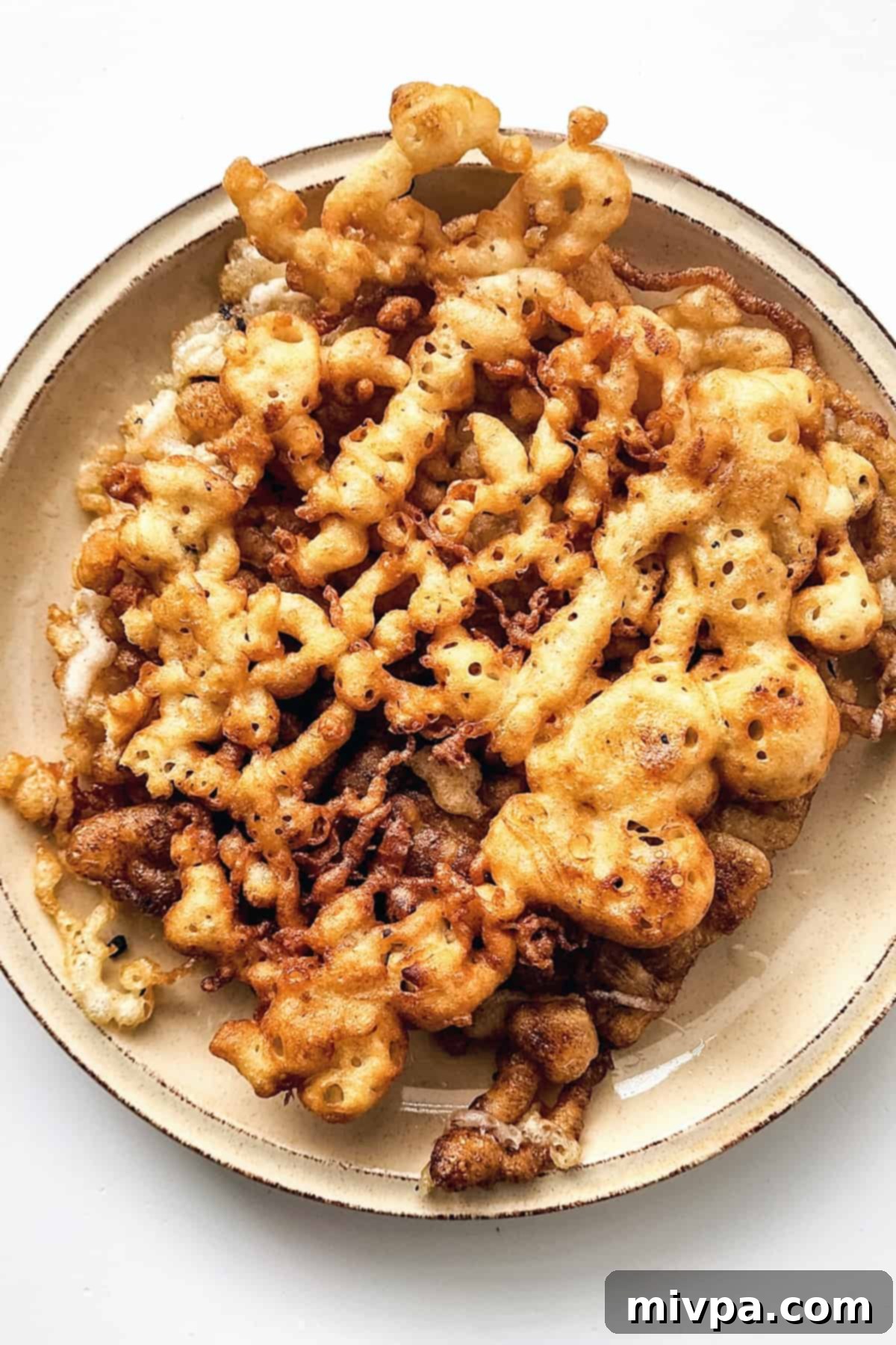 Freshly fried gluten-free funnel cake resting on a plate after being removed from the oil.