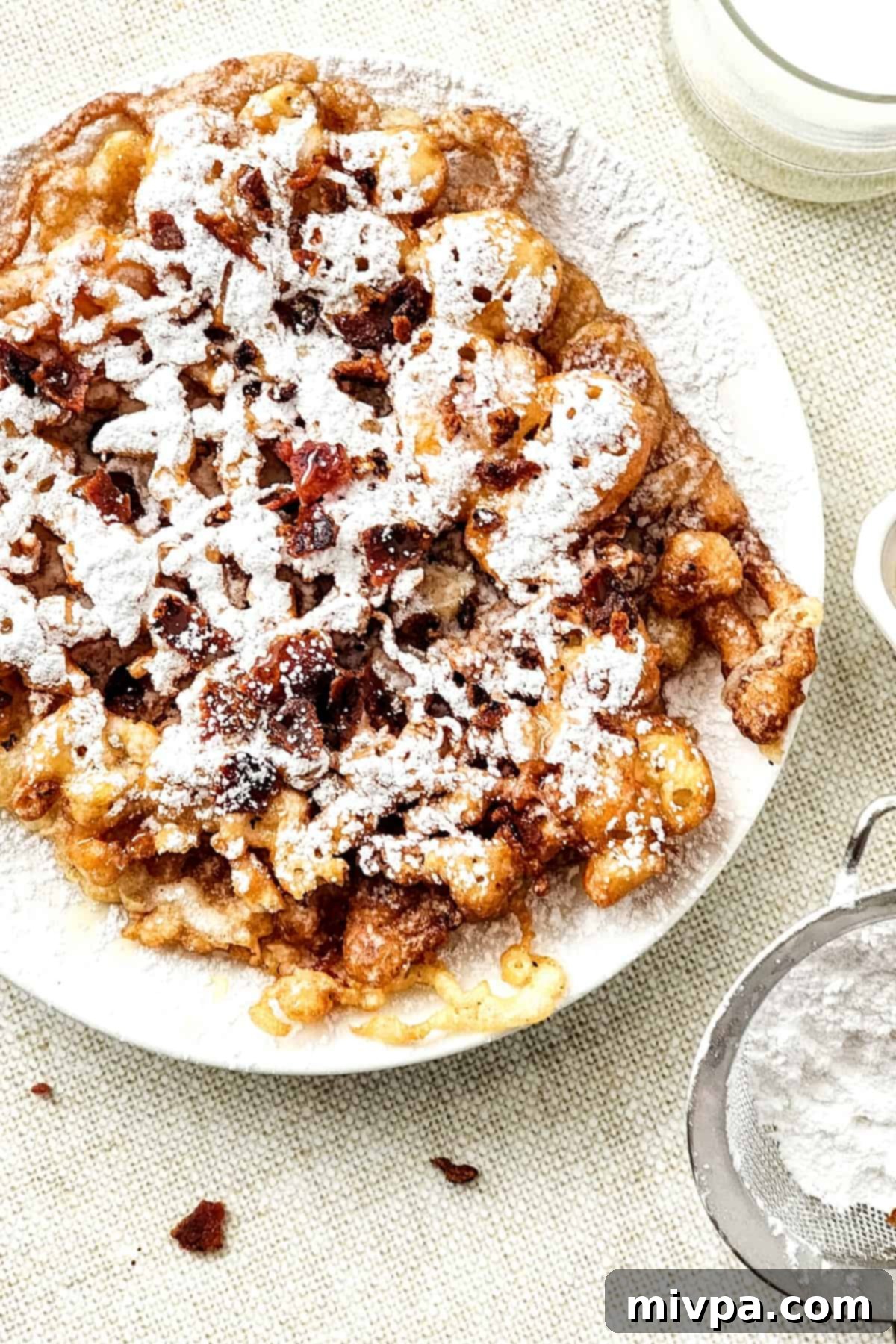 Top down view of a delectable gluten-free funnel cake generously sprinkled with powdered sugar.