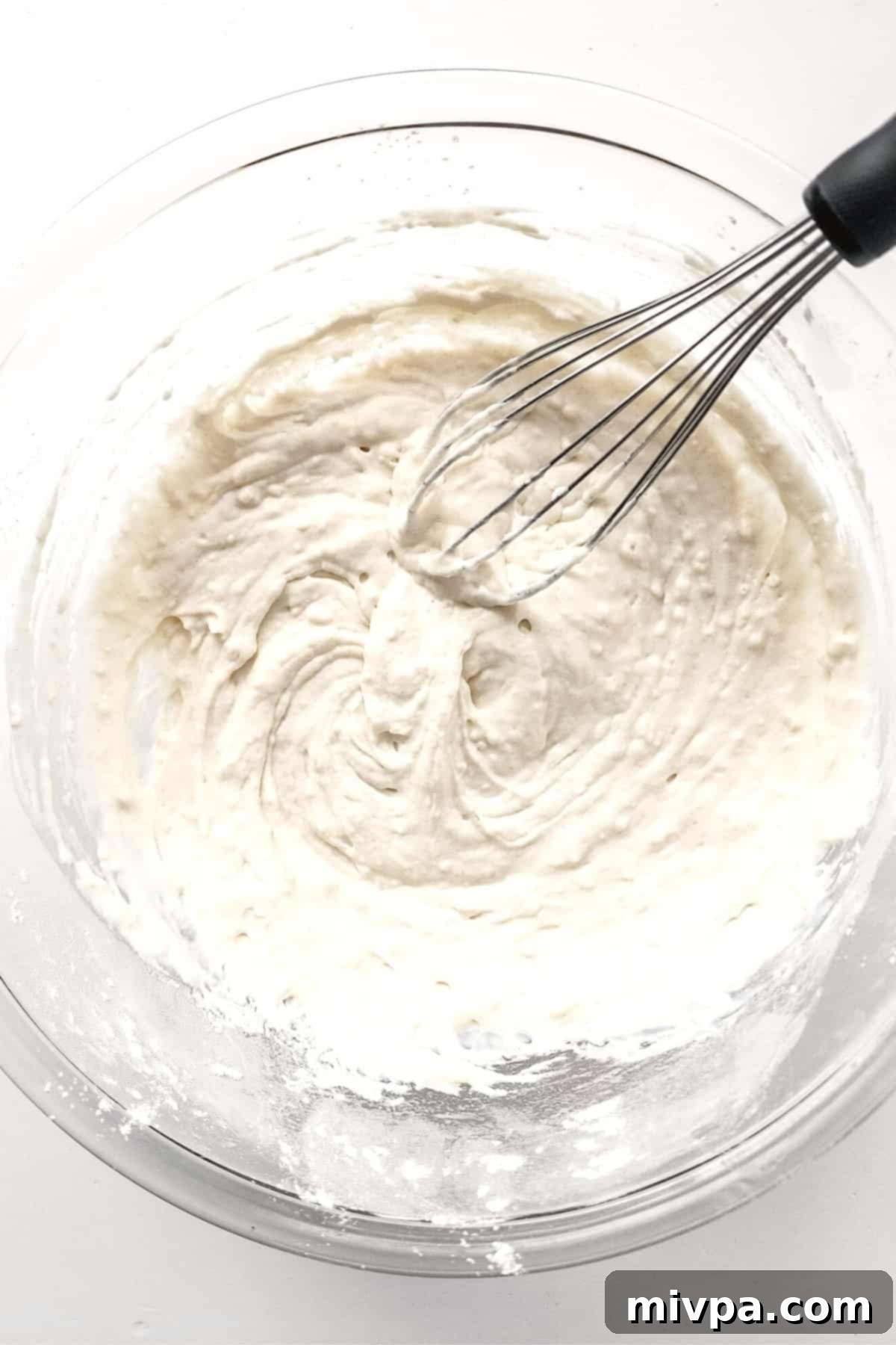 Mixing the gluten-free funnel cake batter in a glass mixing bowl until smooth.