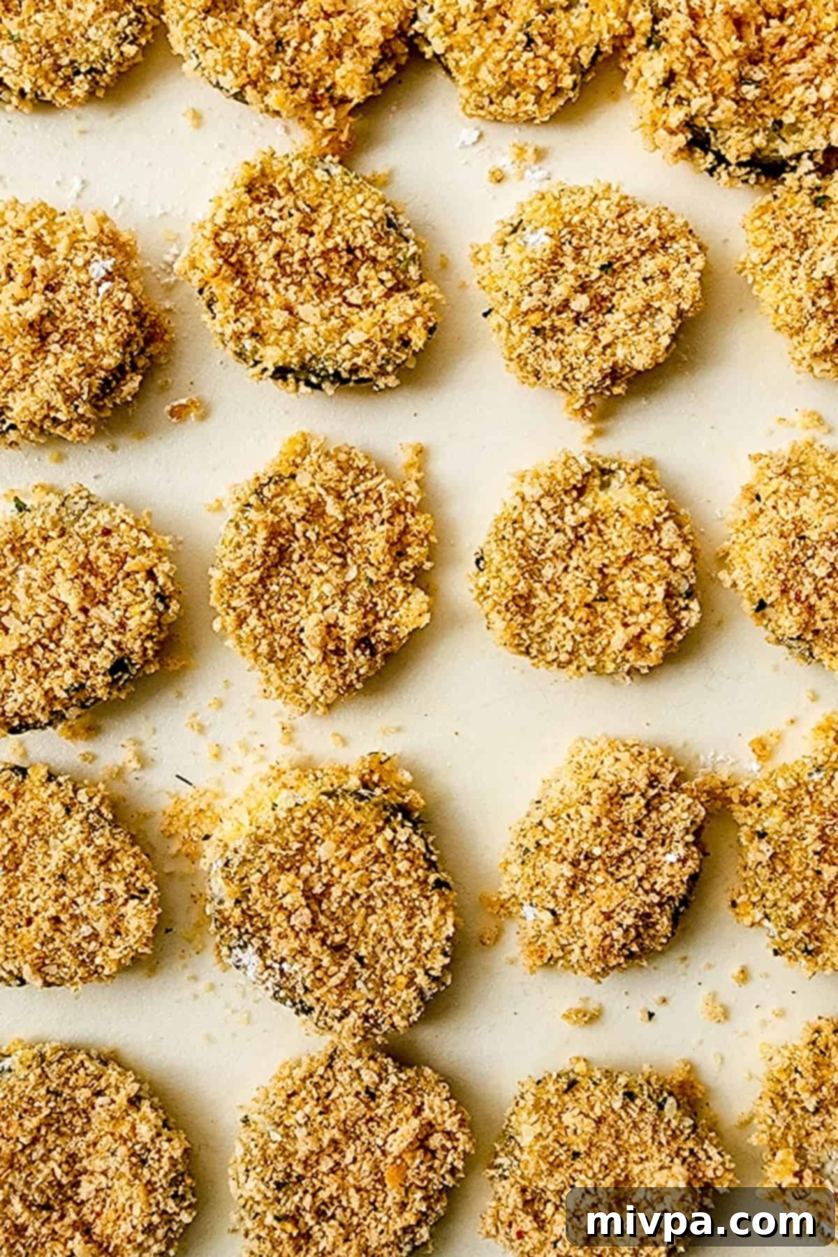 A batch of breadcrumb-coated dill pickle slices neatly arranged on a cutting board, ready for frying.