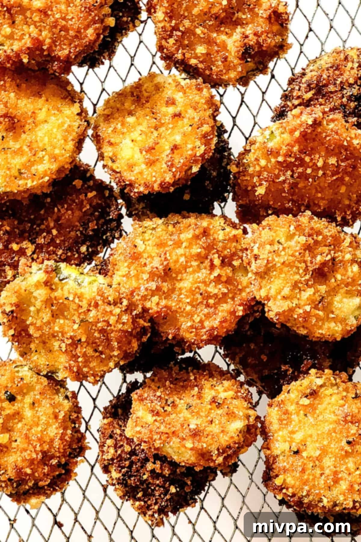A batch of crispy fried pickles resting on a wire rack to drain excess oil, looking perfectly golden brown.