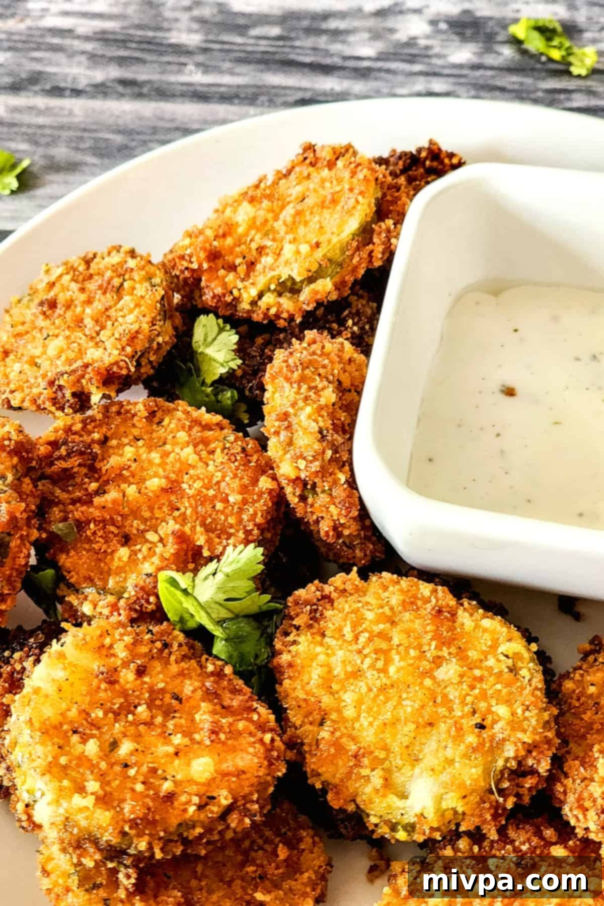 A plate of perfectly golden brown and crispy gluten-free fried pickles, garnished with fresh dill.