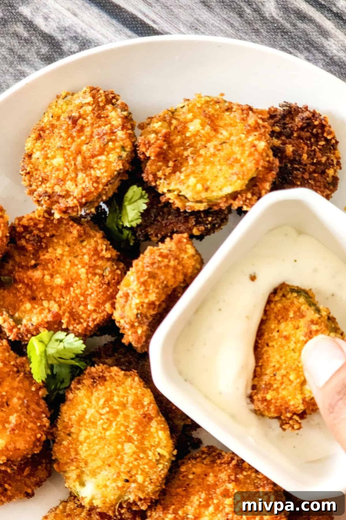 A close-up of a hand dipping a crispy fried pickle into a bowl of creamy ranch dressing.