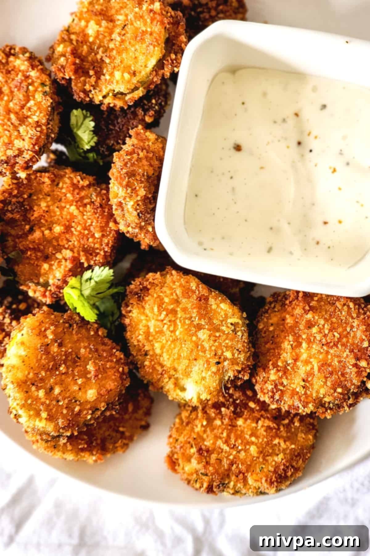 Top down view of a plate piled high with golden-brown fried dill pickle chips, garnished with fresh herbs.