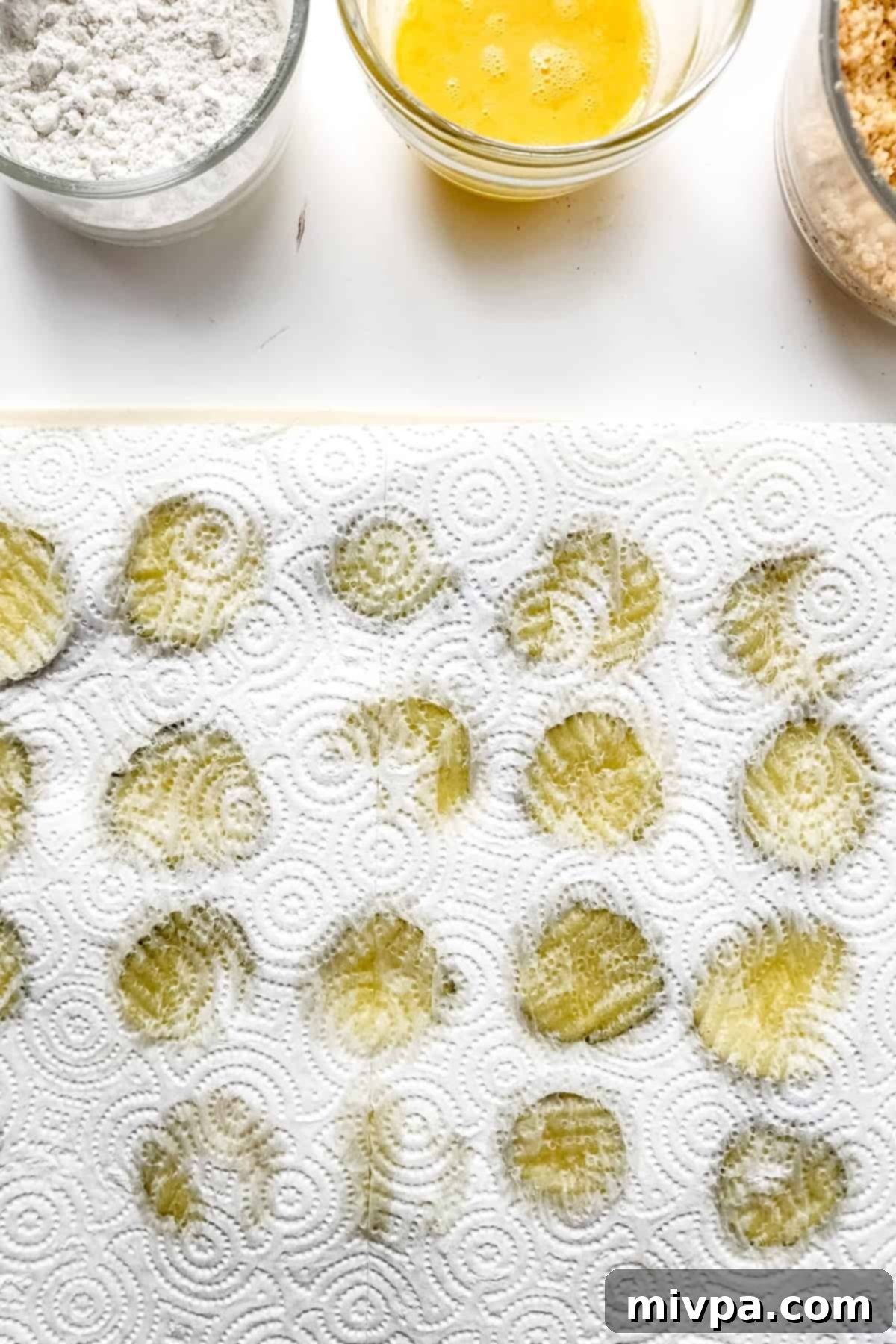 Dill pickle slices being patted dry with paper towels on a cutting board, removing excess moisture.