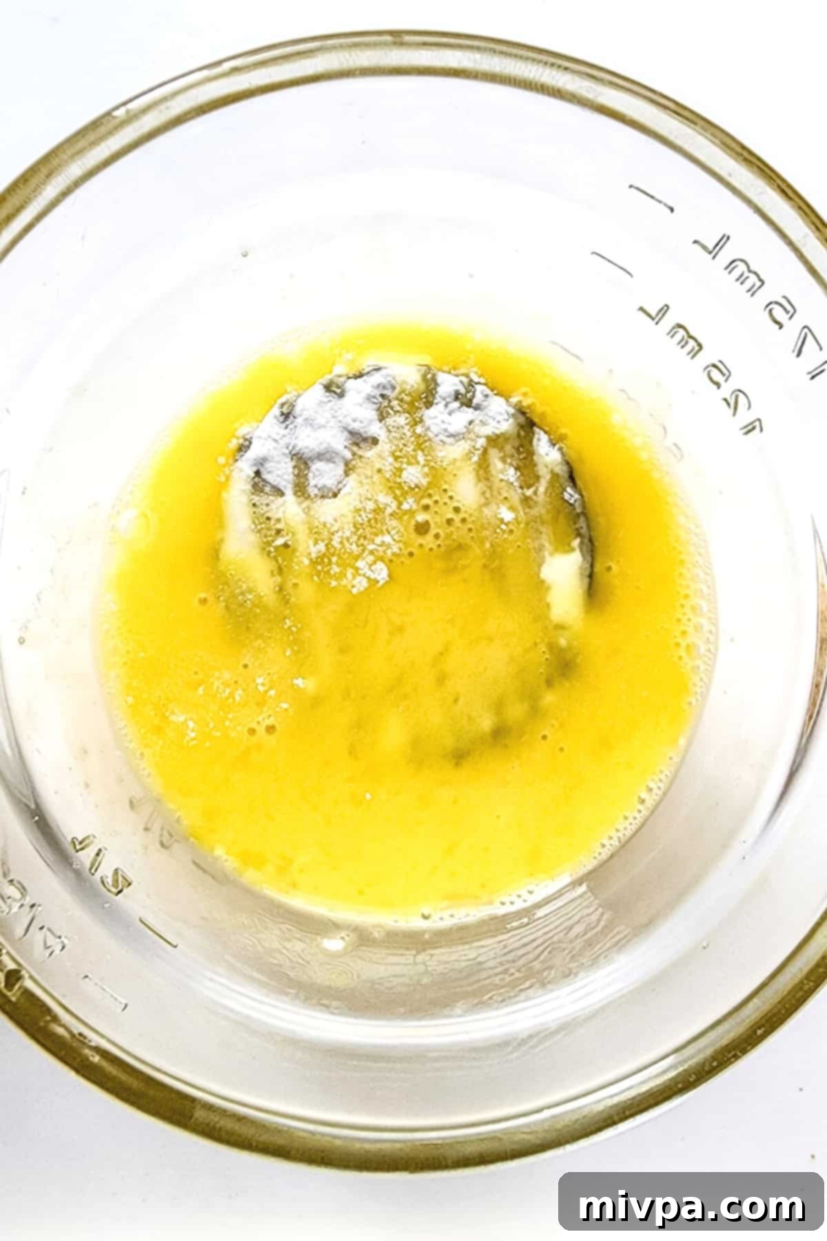 A flour-coated pickle slice being dipped into a bowl of whisked egg.