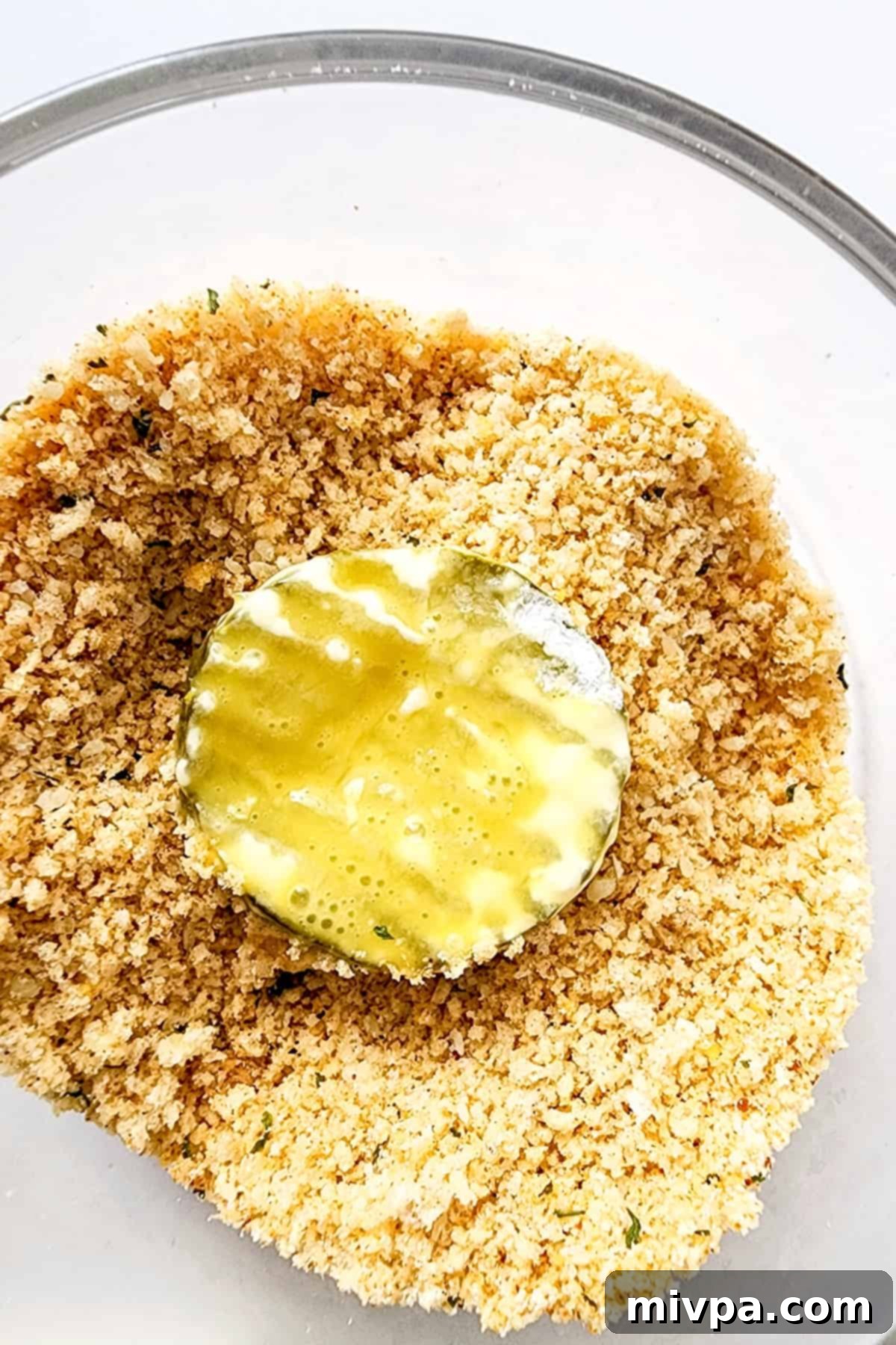 A hand pressing the Parmesan-panko breadcrumb mixture onto an egg-dipped dill pickle slice, ensuring a thick coating.